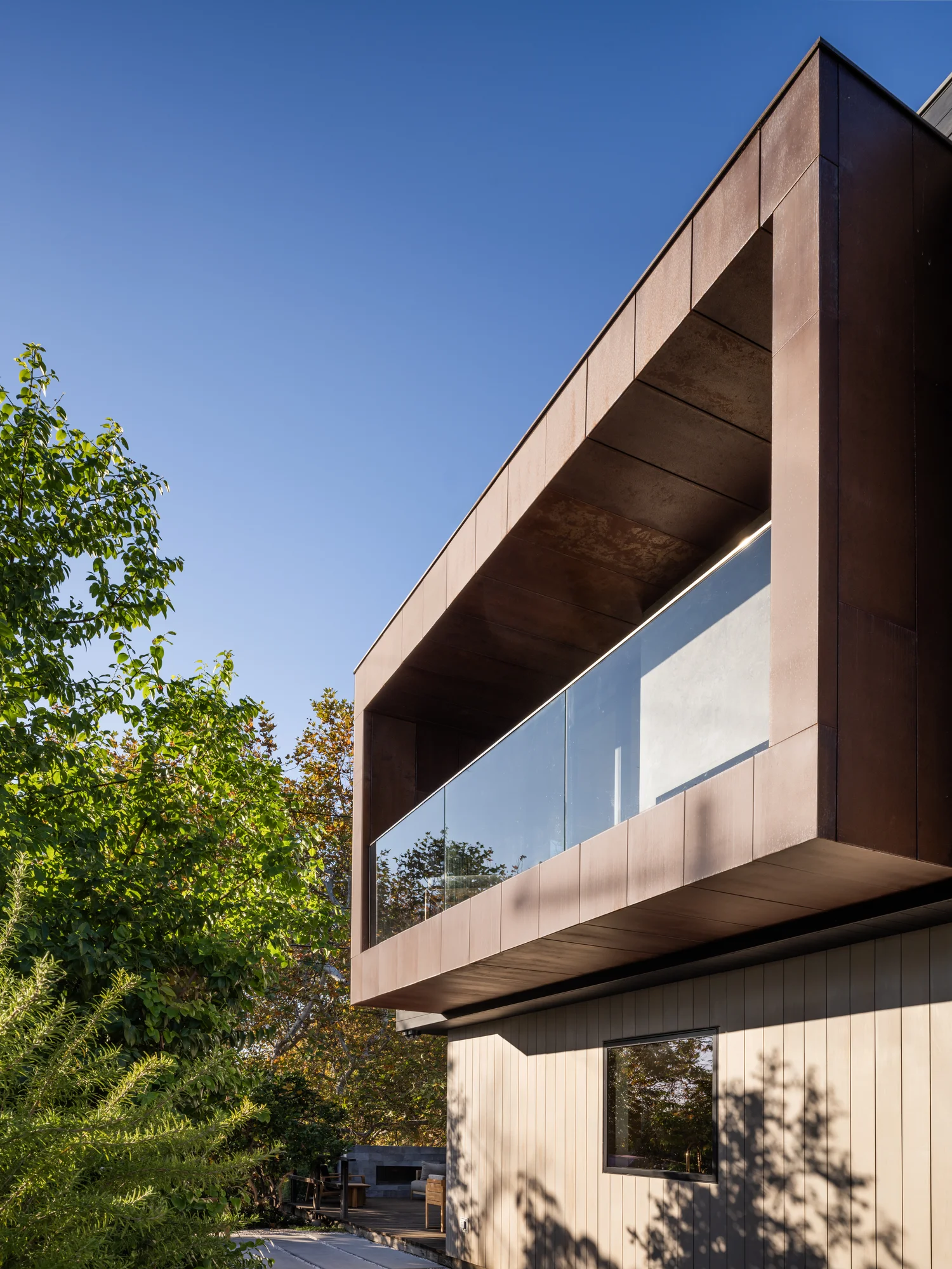 Modern two-story home with cantilevered upper level in bronze metal cladding and cedar-clad lower level surrounded by trees