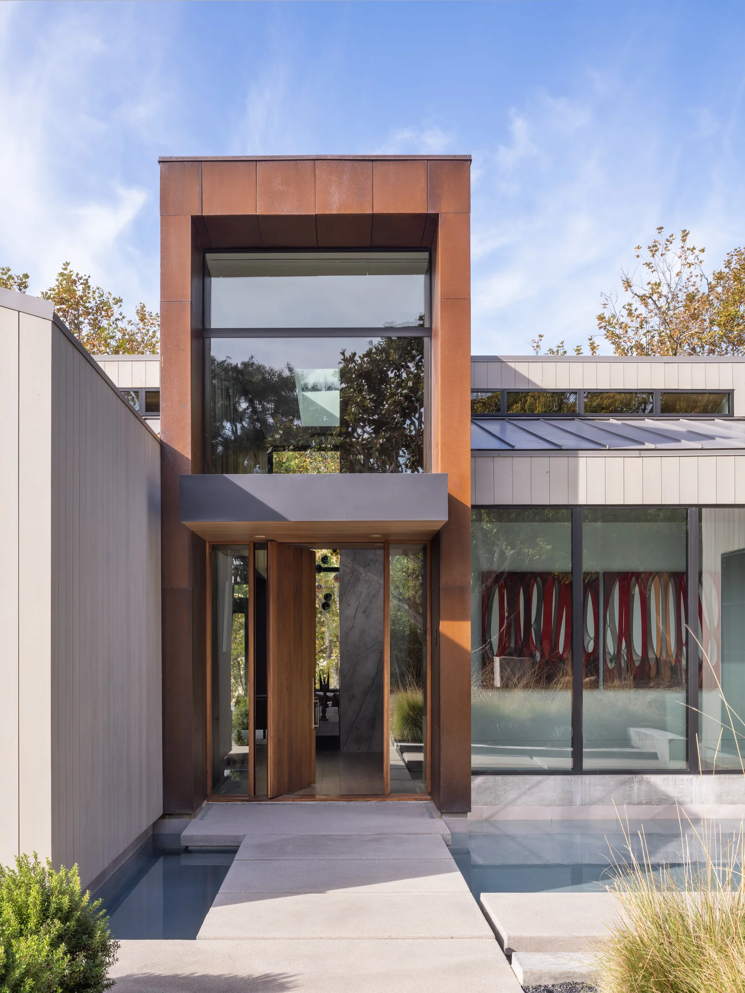 Modern home entrance with copper-clad tower, wooden doors, and water feature connecting indoor-outdoor spaces.