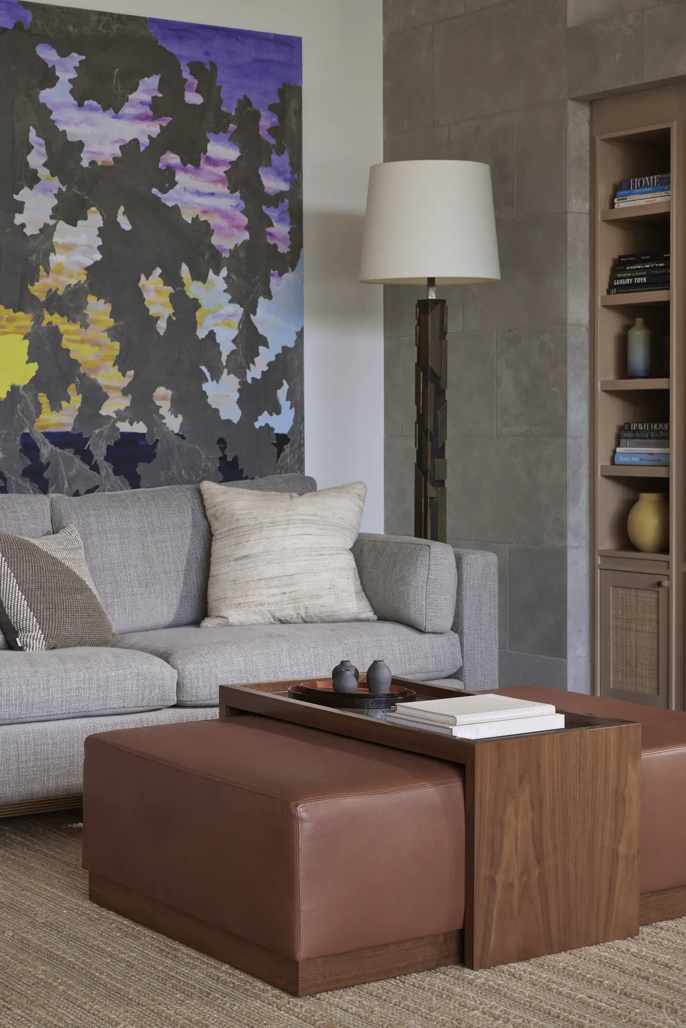 Modern living room with gray sofa, walnut coffee table, abstract painting, and built-in shelving with natural textures.