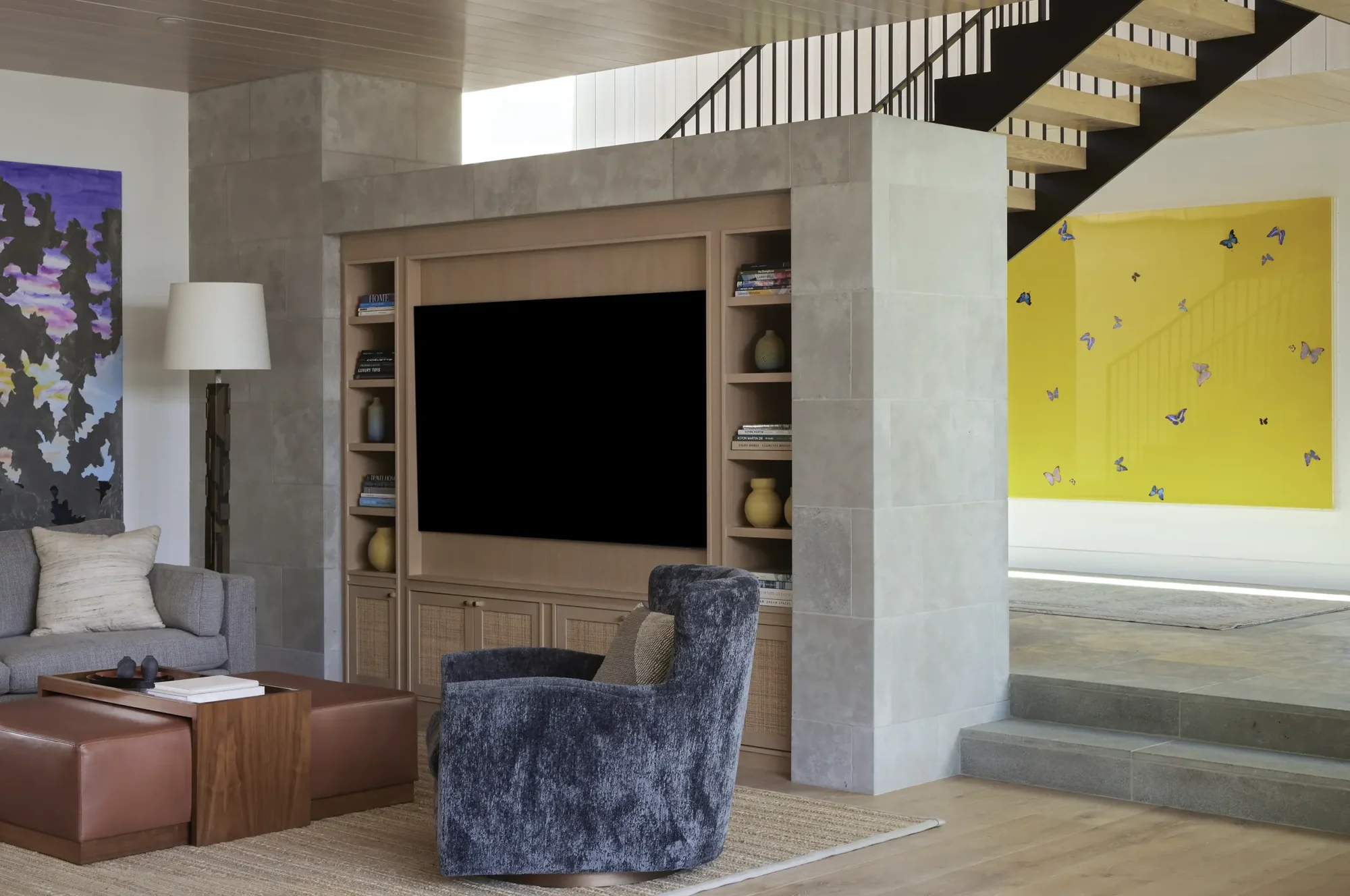 Modern living room with built-in entertainment center, floating staircase, and yellow butterfly artwork