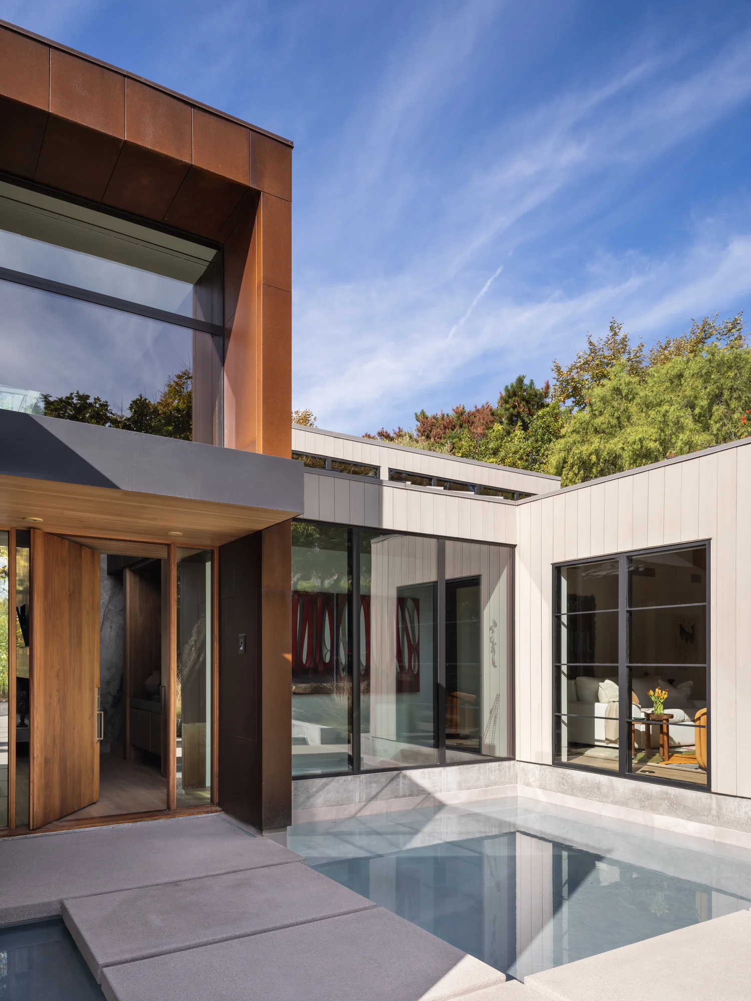 Modern home exterior with copper cladding, white vertical siding, pool, and large glass doors opening to courtyard.