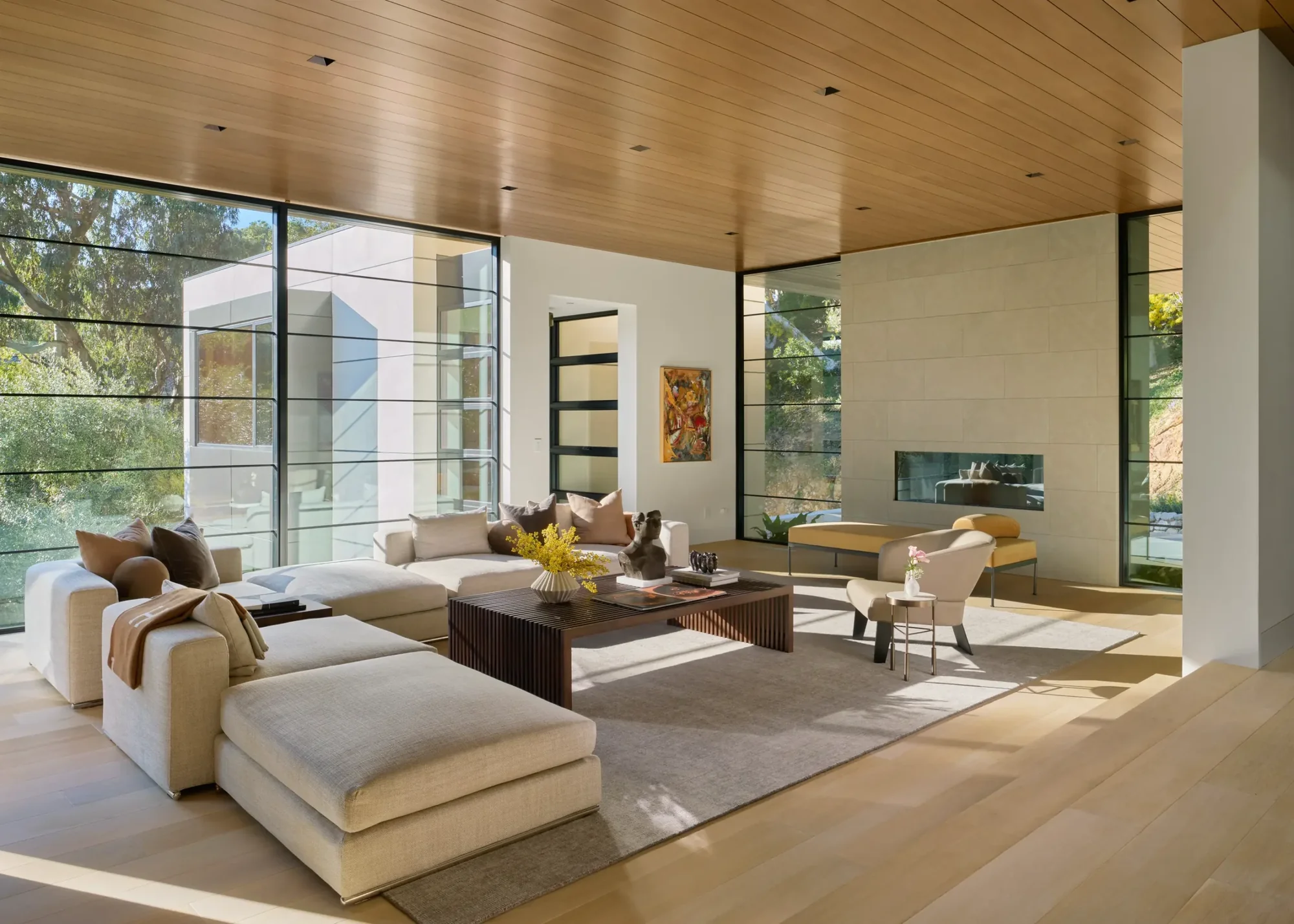 Modern living room with wood ceiling, floor-to-ceiling windows, cream sectional sofa, and seamless indoor-outdoor connection.