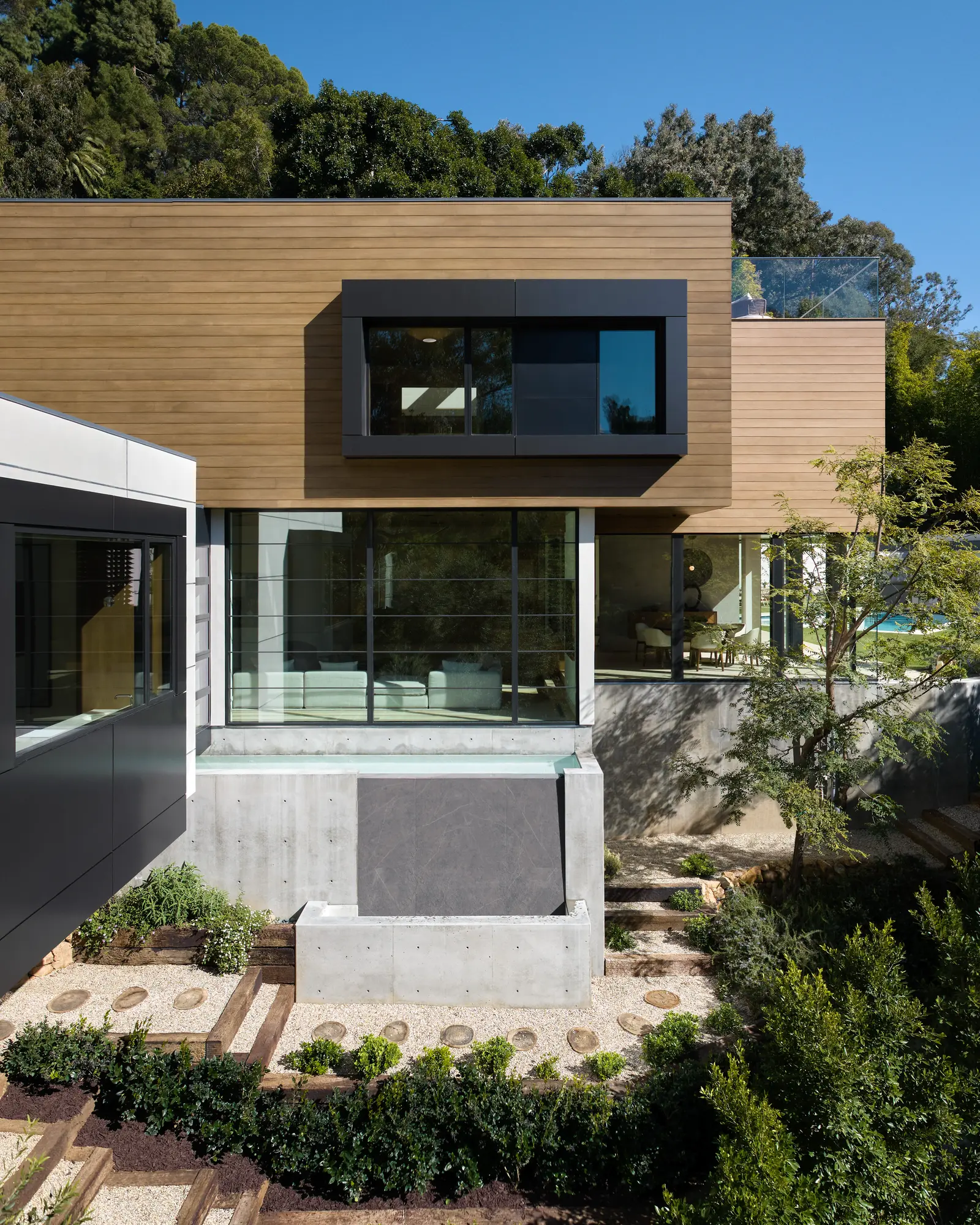 Modern two-story home with horizontal cedar siding, dark metal cantilevered window box, and exposed concrete foundation