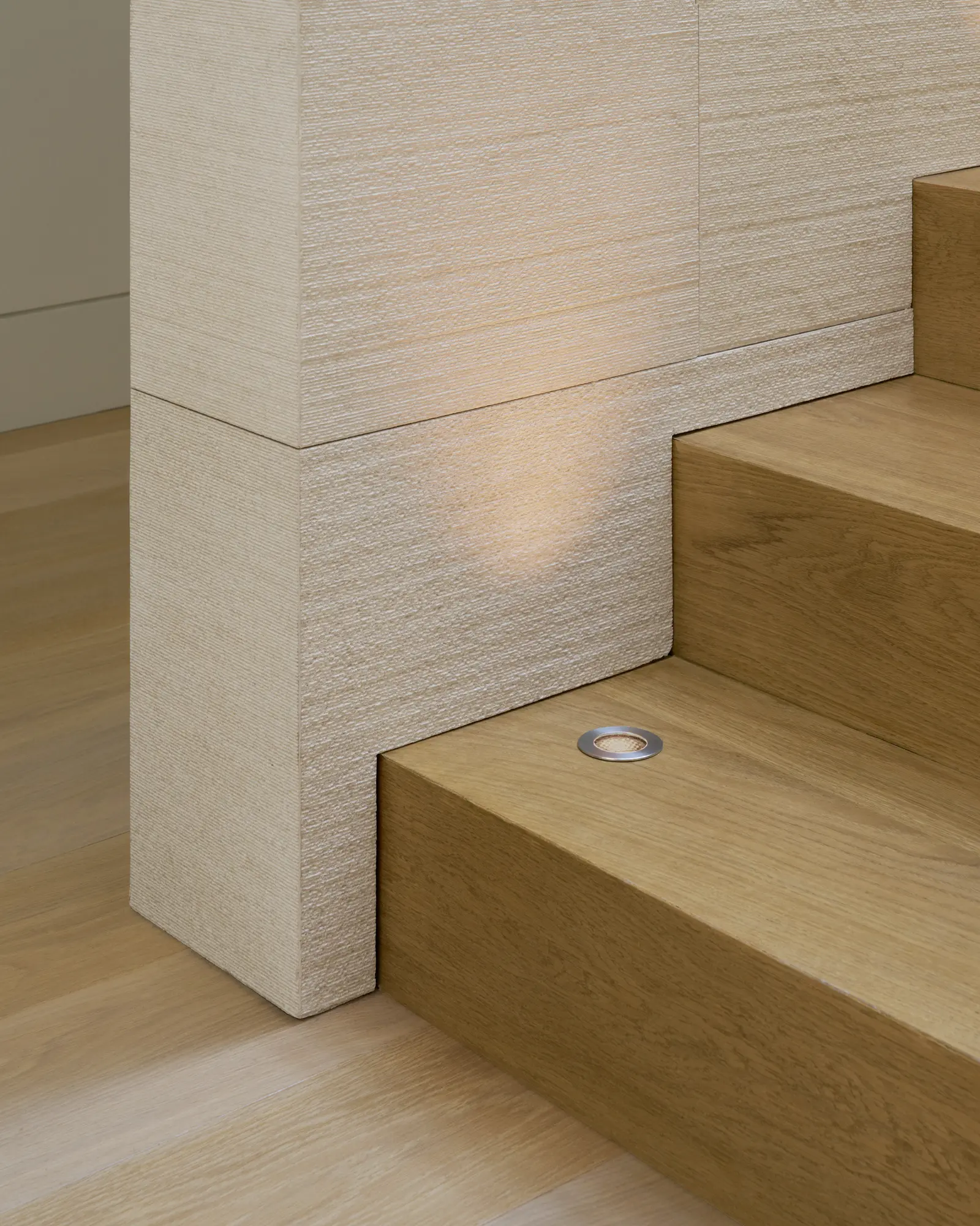Natural oak stair treads with integrated lighting meet textured white wall panels in modern architectural detail