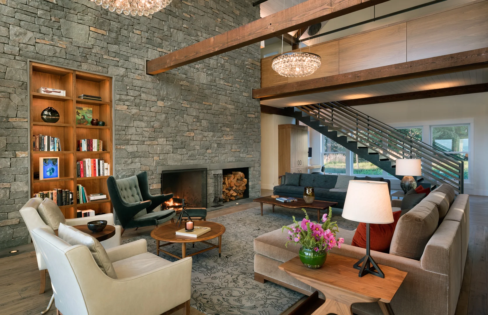 Double-height living room with gray stone wall, fireplace, built-in shelving, and open staircase to upper level
