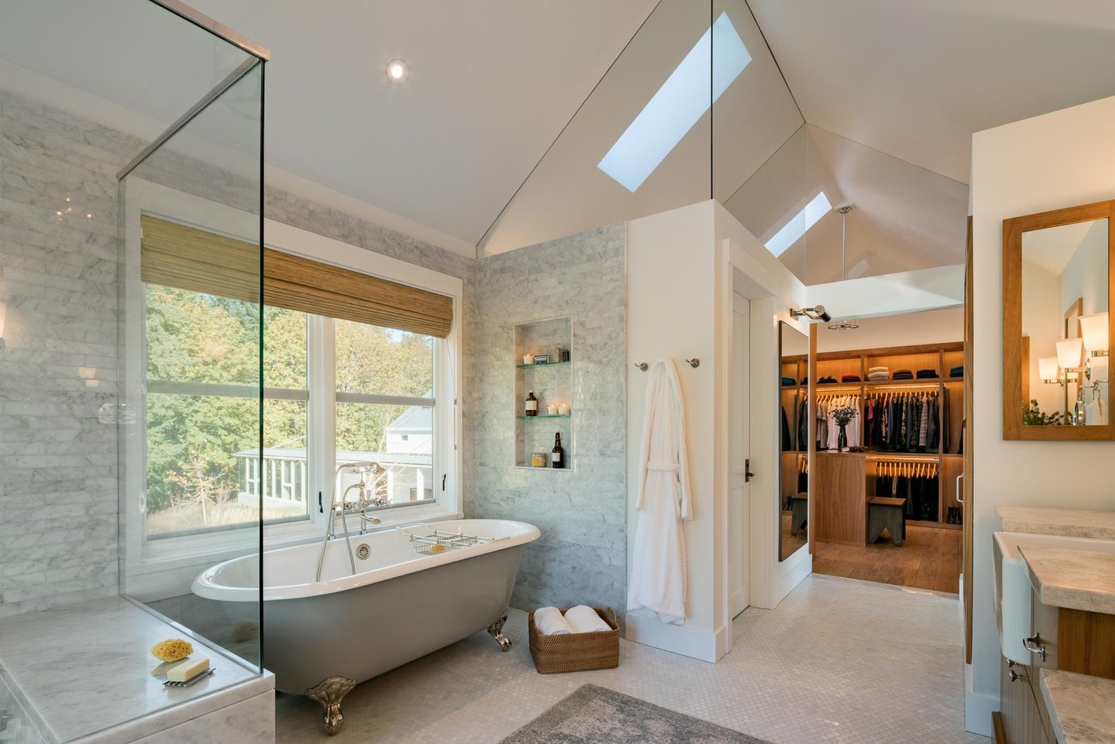 Luxury master bathroom with freestanding clawfoot tub, marble walls, skylights, and adjoining walk-in closet