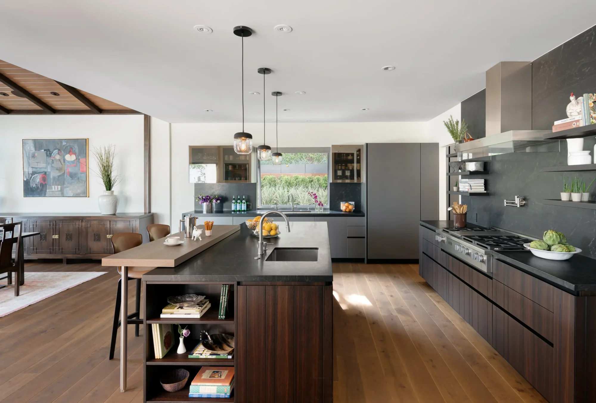 Modern open-plan kitchen with dark gray cabinetry, wood island, and pendant lights connecting to dining area