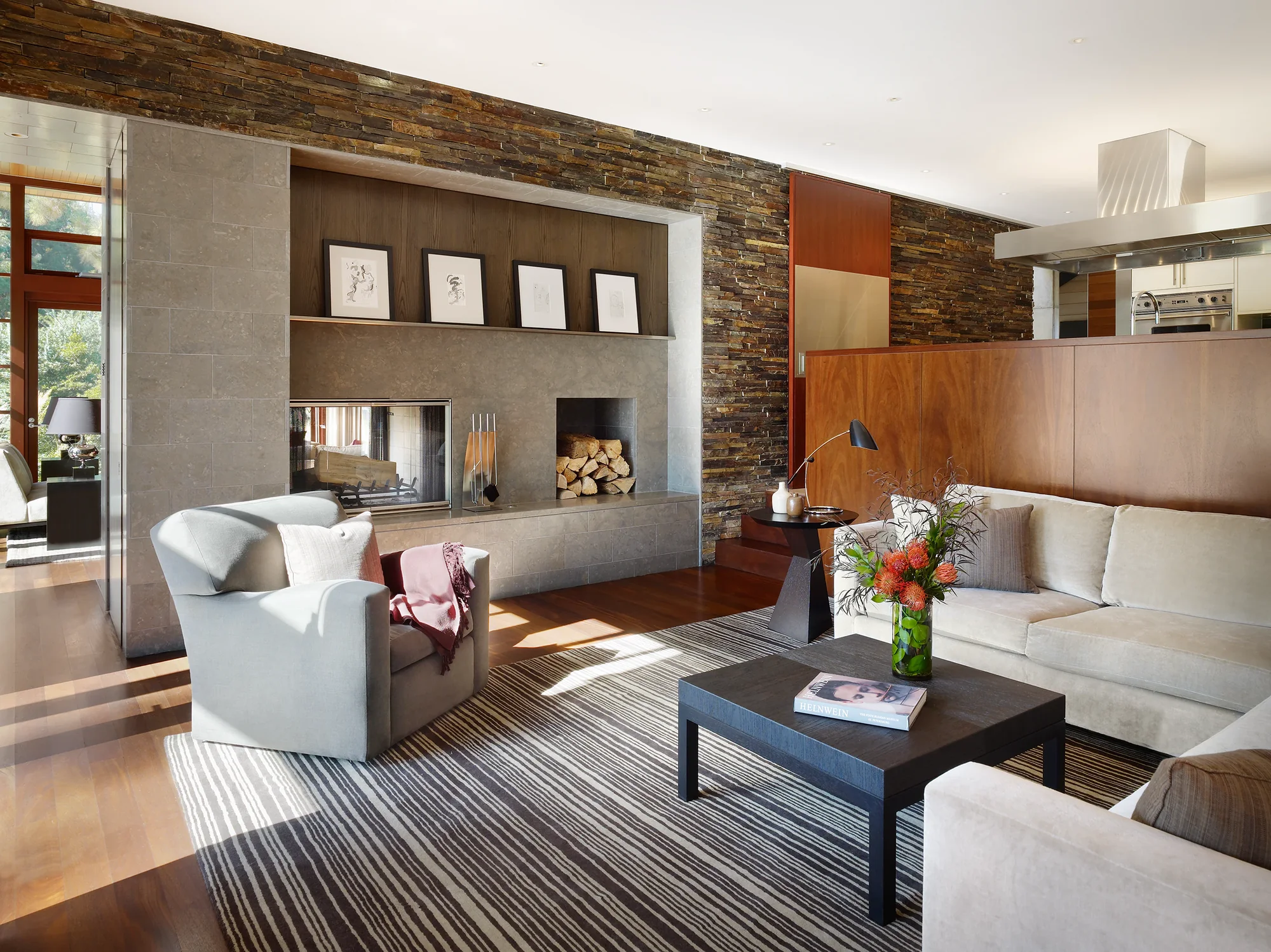 Modern living room with stone fireplace, striped rug, and wood accent wall connecting to open kitchen