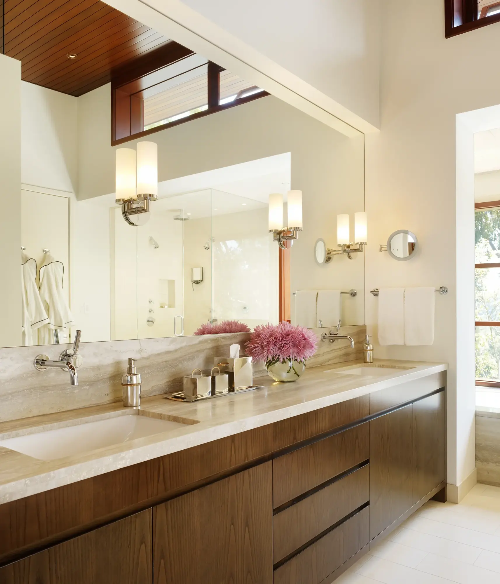 Modern bathroom vanity with natural stone countertop, wood cabinetry, and vaulted ceiling with clerestory windows