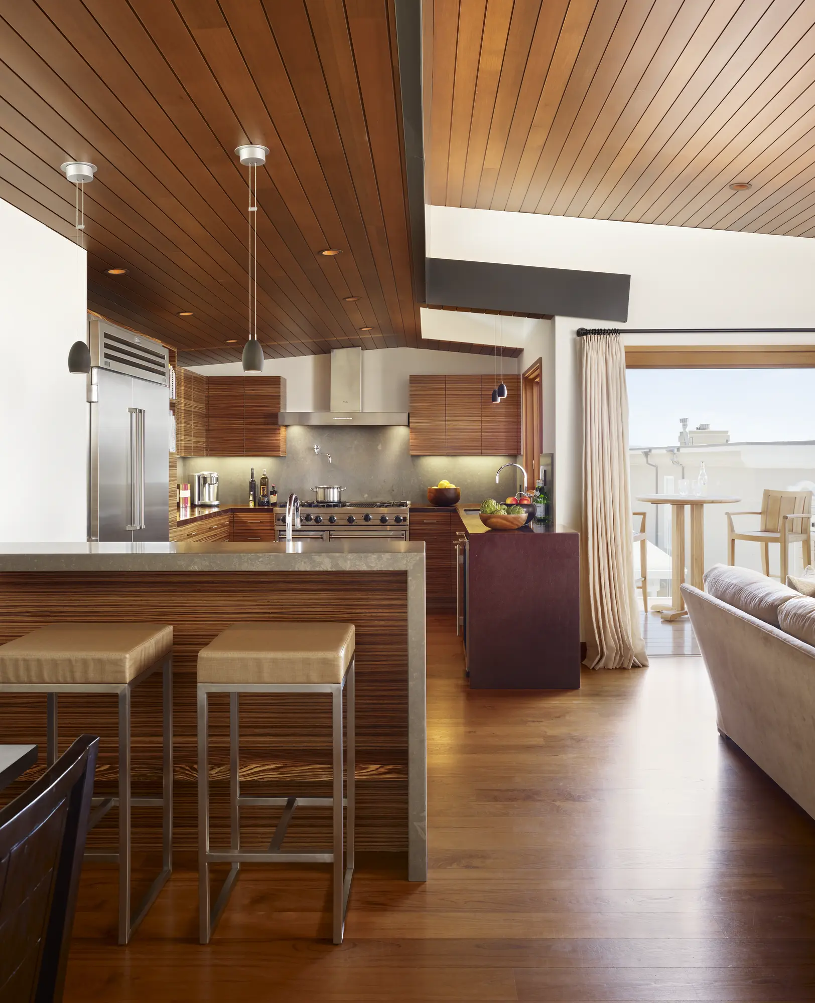 Modern kitchen with wood-slatted ceiling, horizontal-grain cabinetry, and open flow to outdoor living space