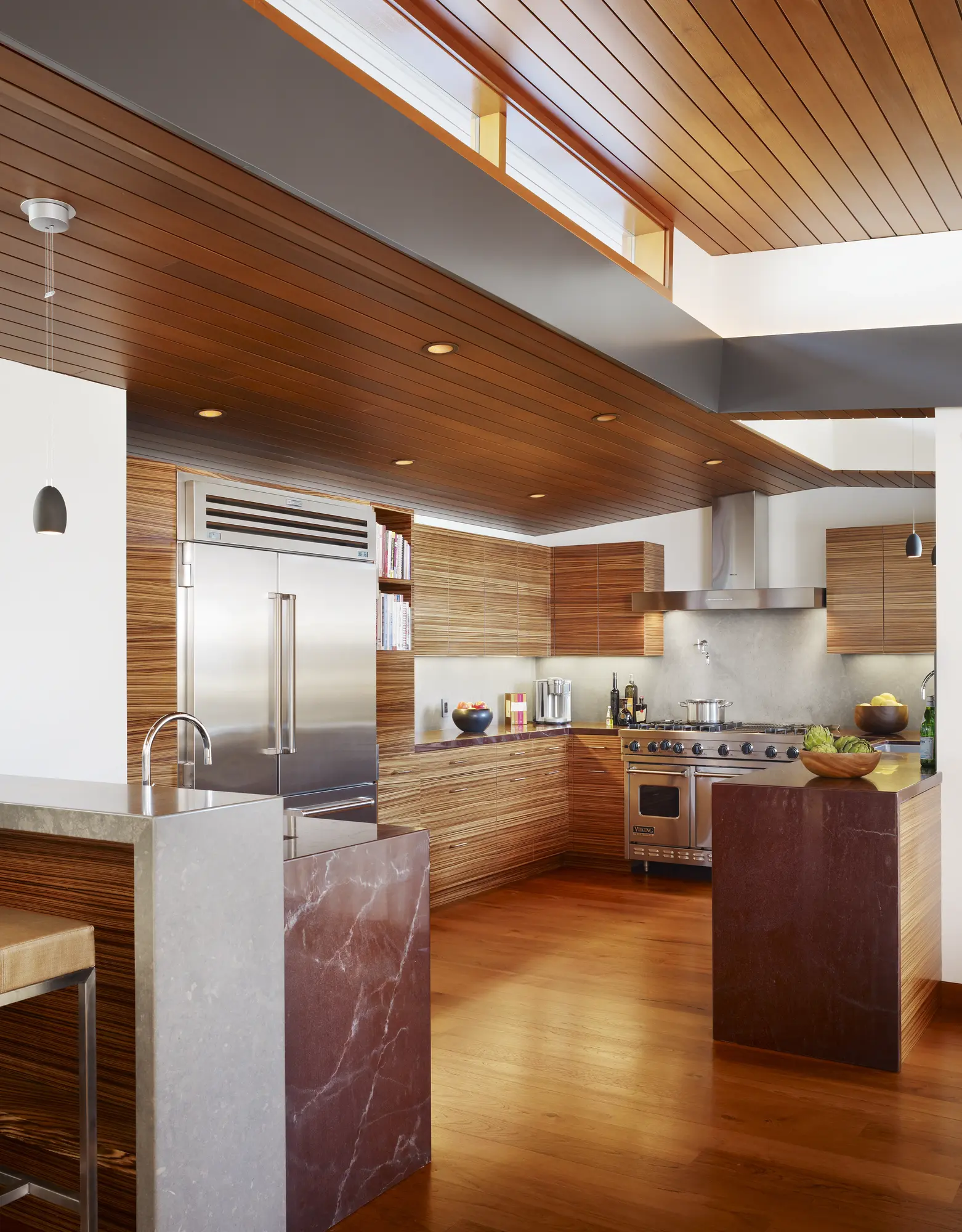 Modern kitchen with horizontal wood cabinetry, marble waterfall island, stainless steel appliances, and wood slat ceiling