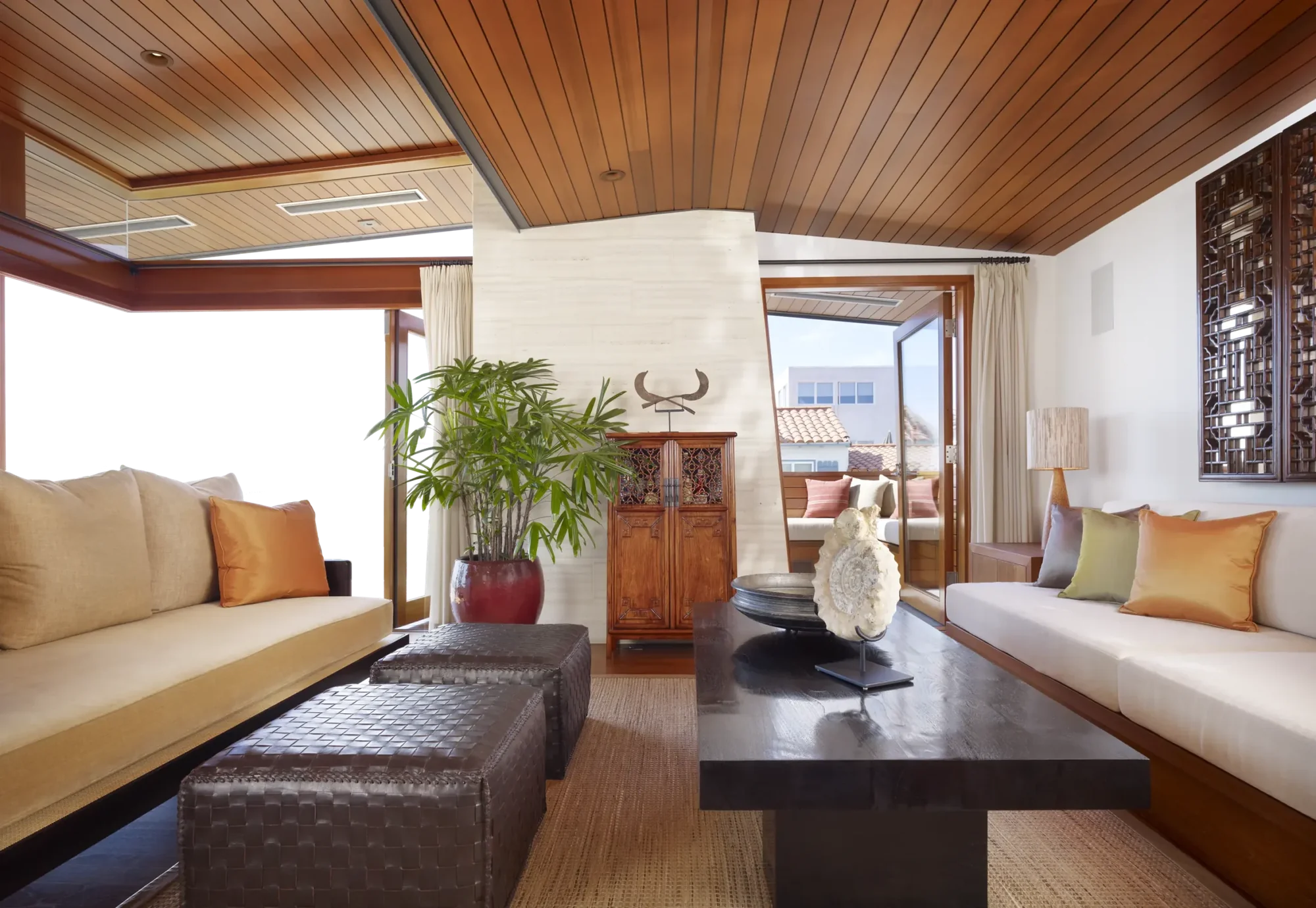 Modern living room with wood ceiling, built-in seating, and views to outdoor terrace through open doorway.