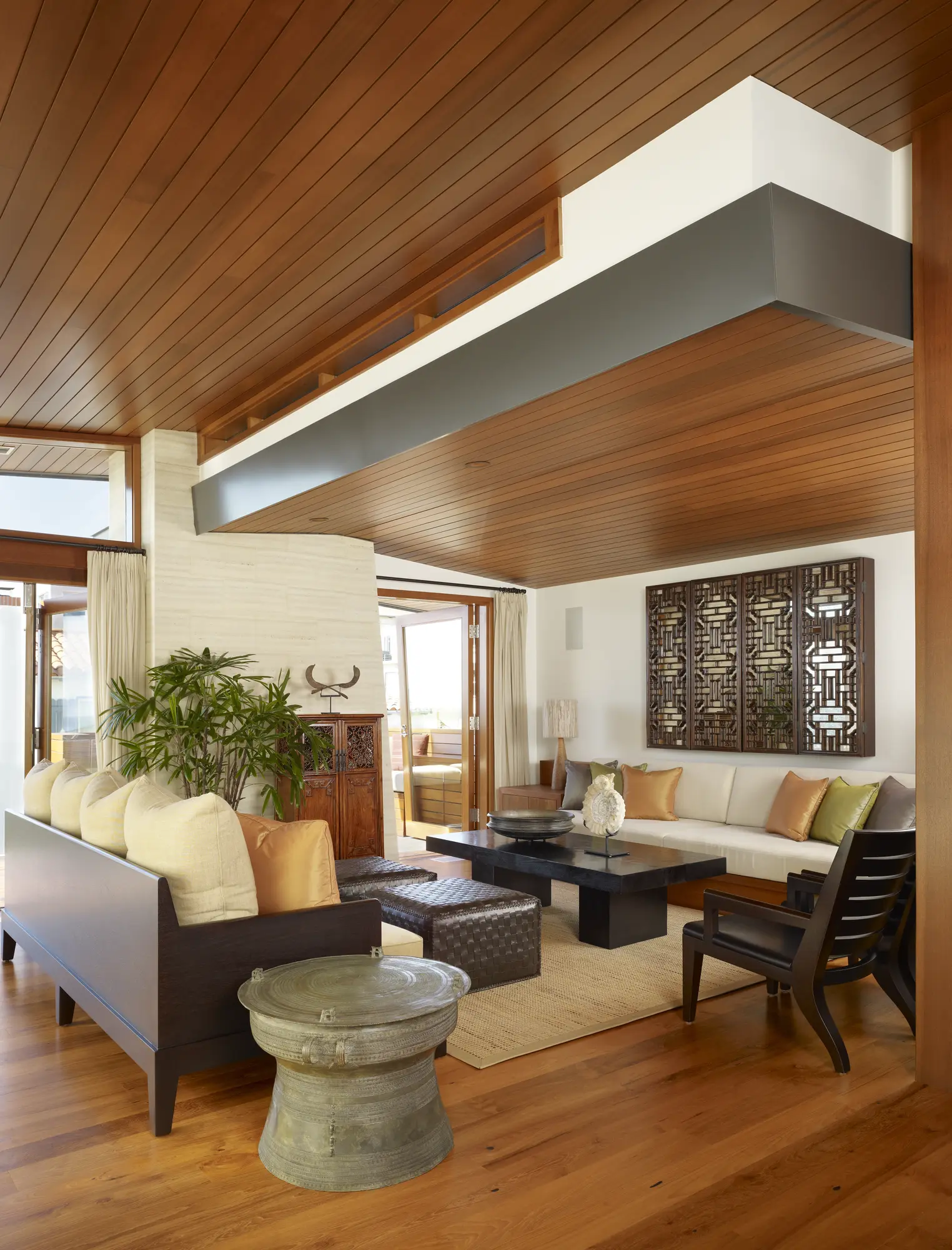 Modern living room with wood ceiling, white beam, Asian-inspired wall art, and natural materials blending indoor-outdoor spaces.