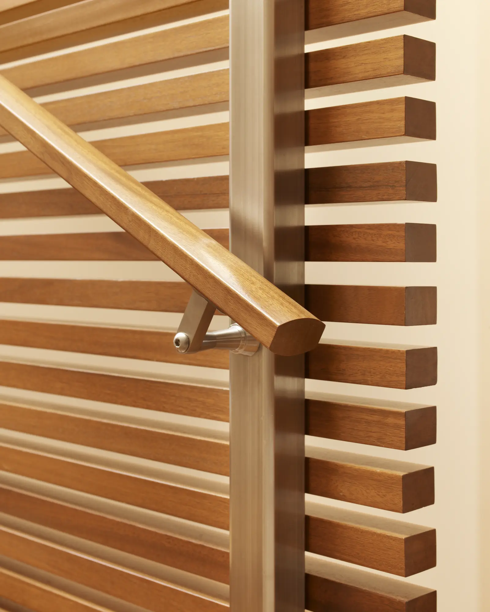 Wooden handrail with brushed metal brackets alongside horizontal wood slat staircase detail