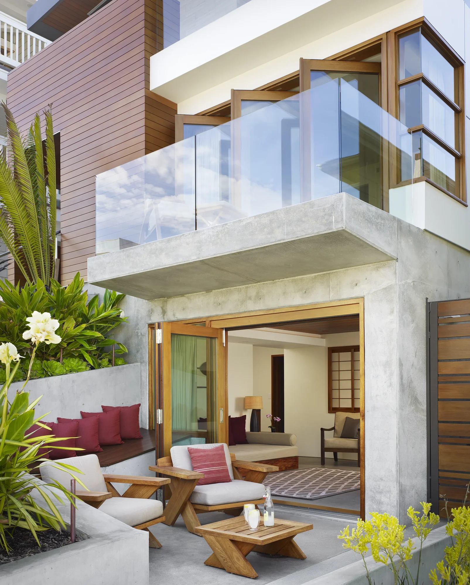 Modern two-story home with concrete structure, wood-framed windows, and outdoor patio blending indoor-outdoor living spaces.