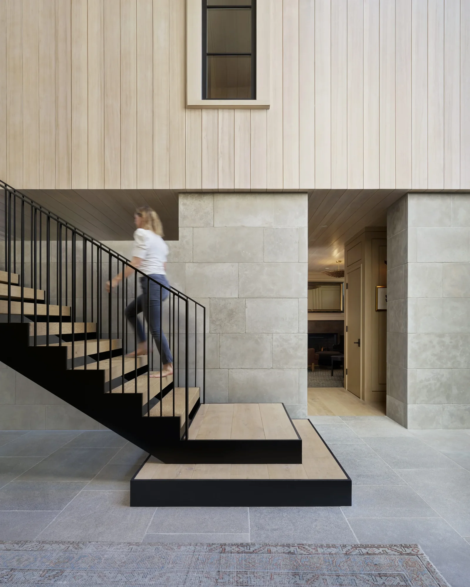 Modern entryway featuring floating staircase with black metal railings, limestone walls, and light wood ceiling