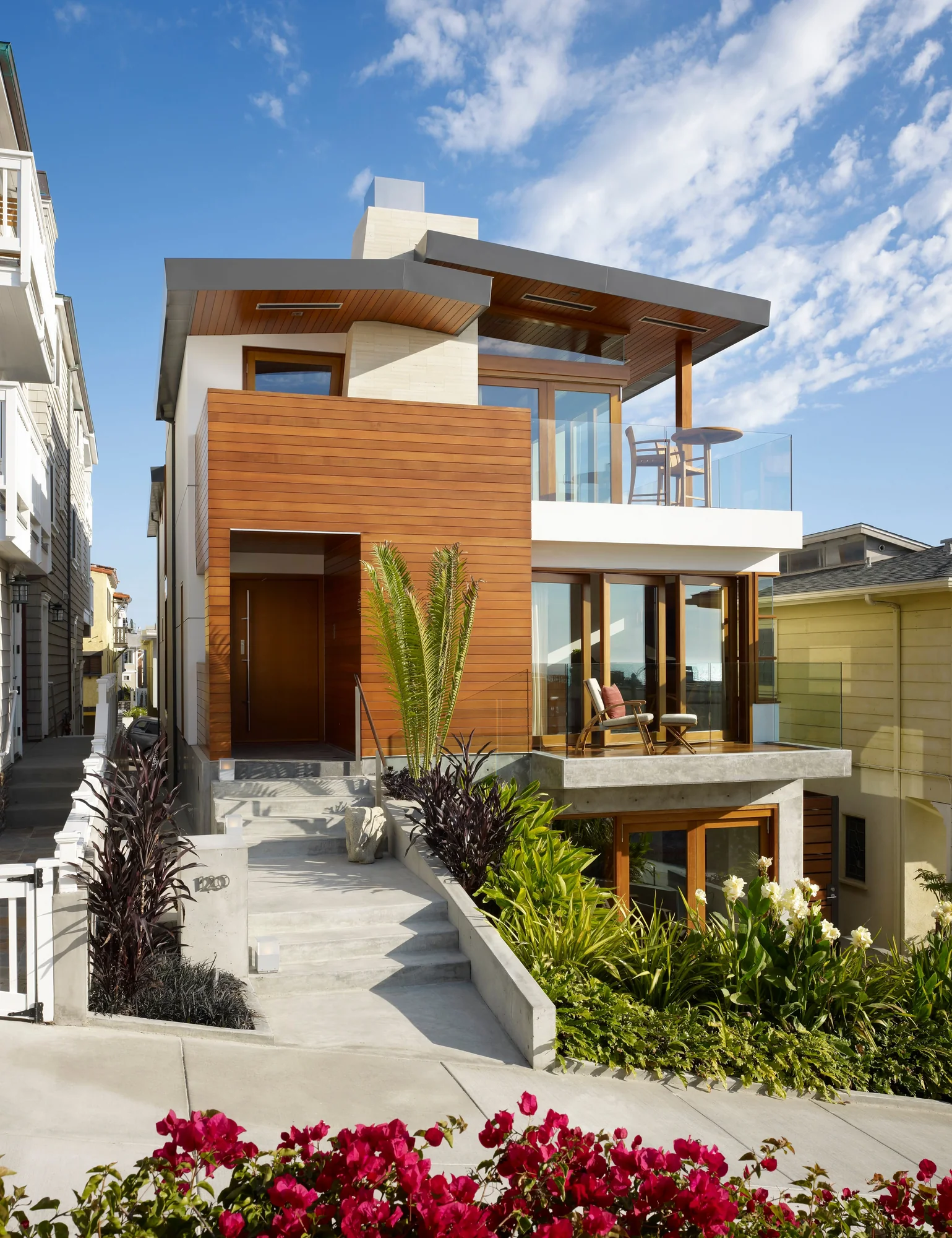 Modern three-story beach house with horizontal cedar siding, white stucco, and expansive glass walls on tiered levels.