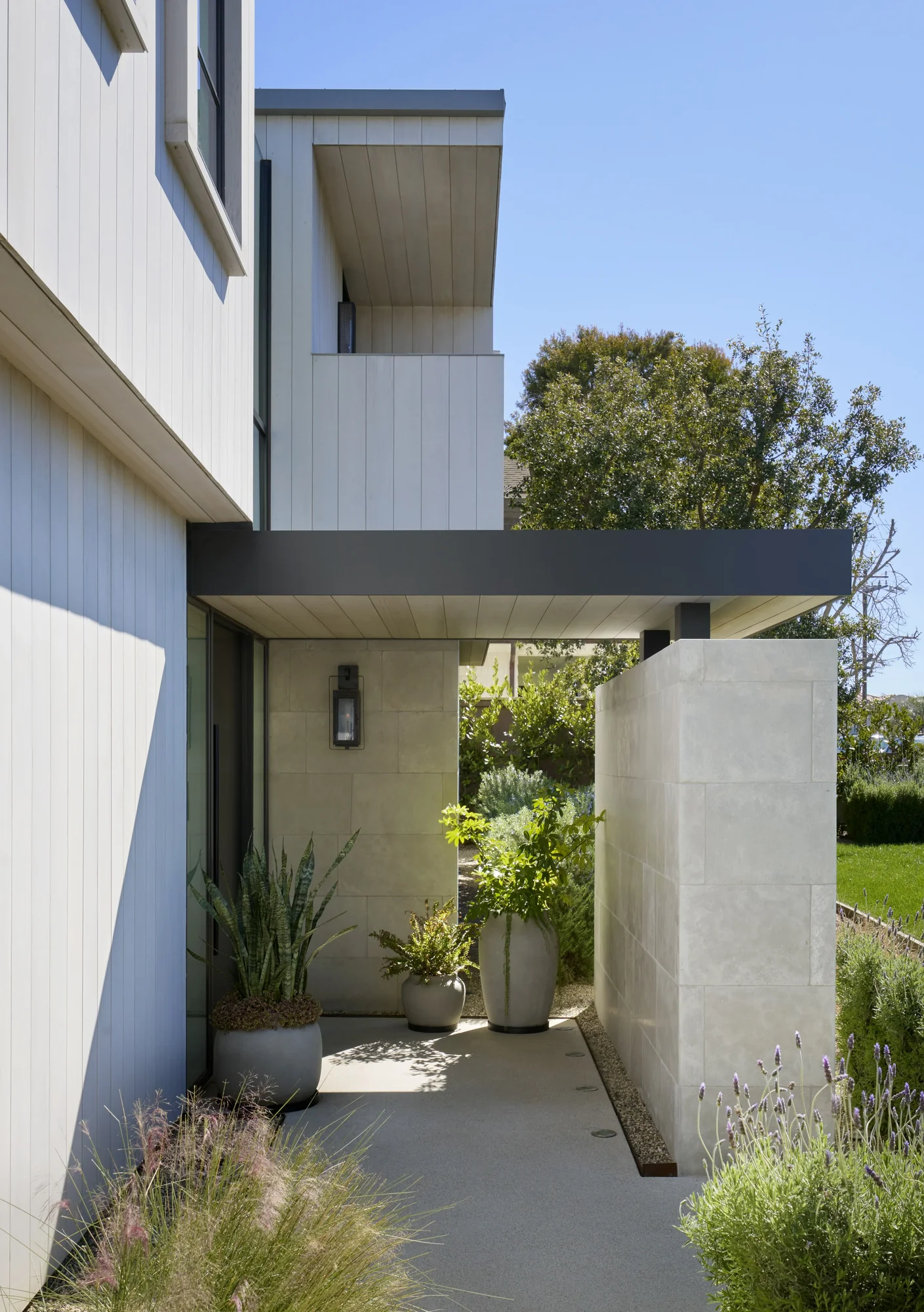 Covered entryway with concrete walls and ceiling, potted plants flanking path, modern farmhouse architecture beyond