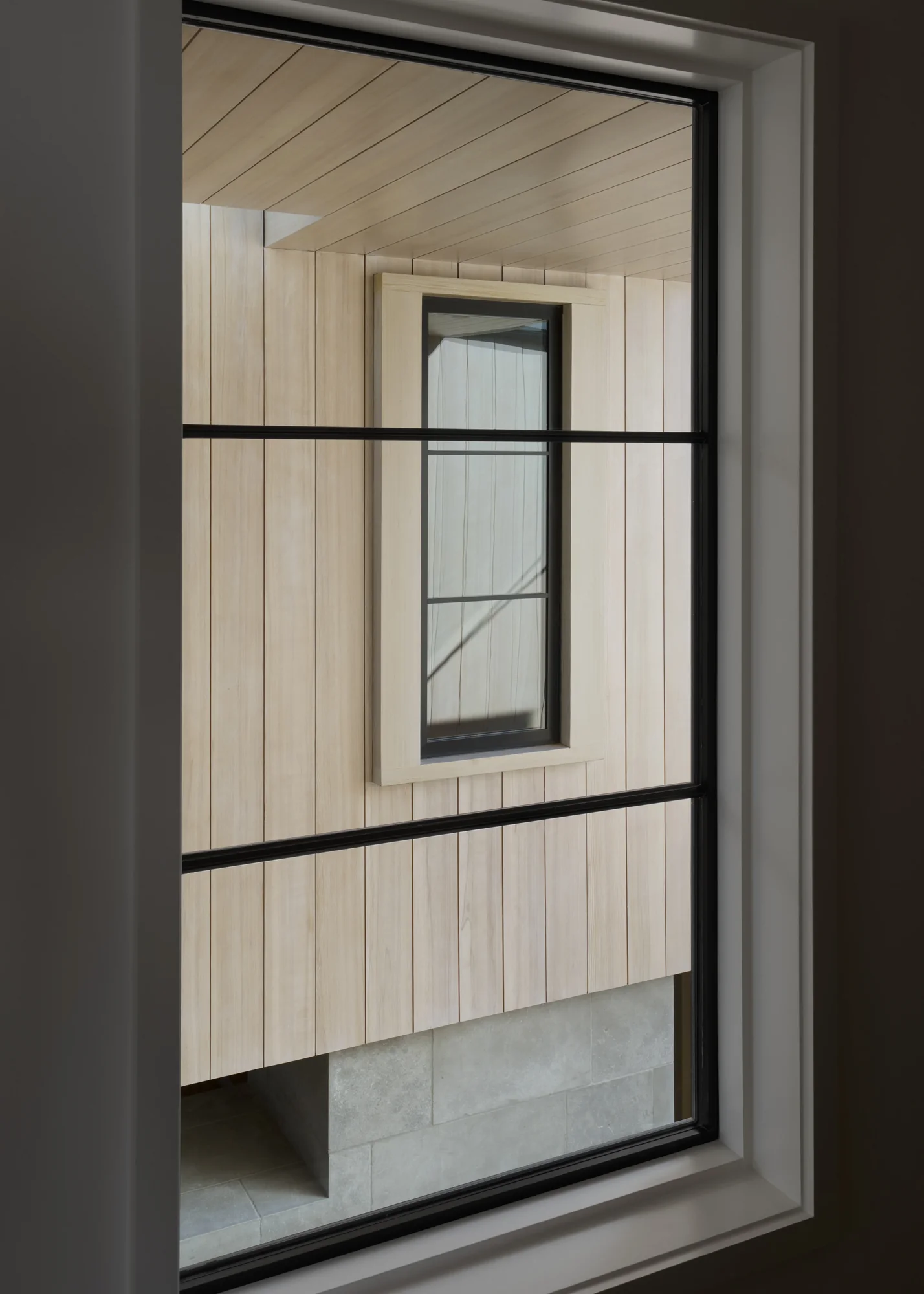 View through black-framed window showing light wood paneled interior with nested window, creating layered depth
