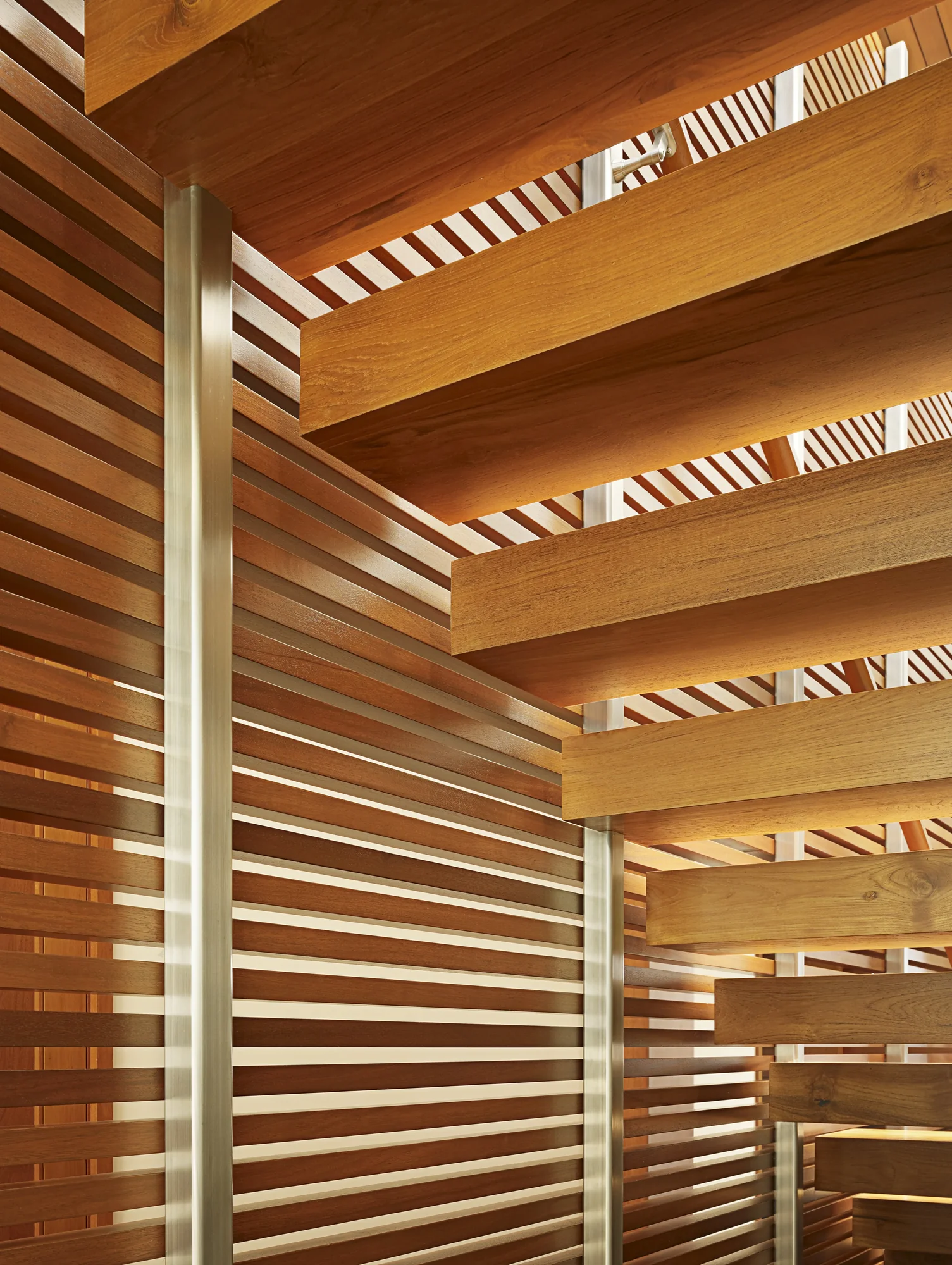 Wooden stairwell with horizontal cedar slats and metal columns, featuring natural light filtering through slatted openings