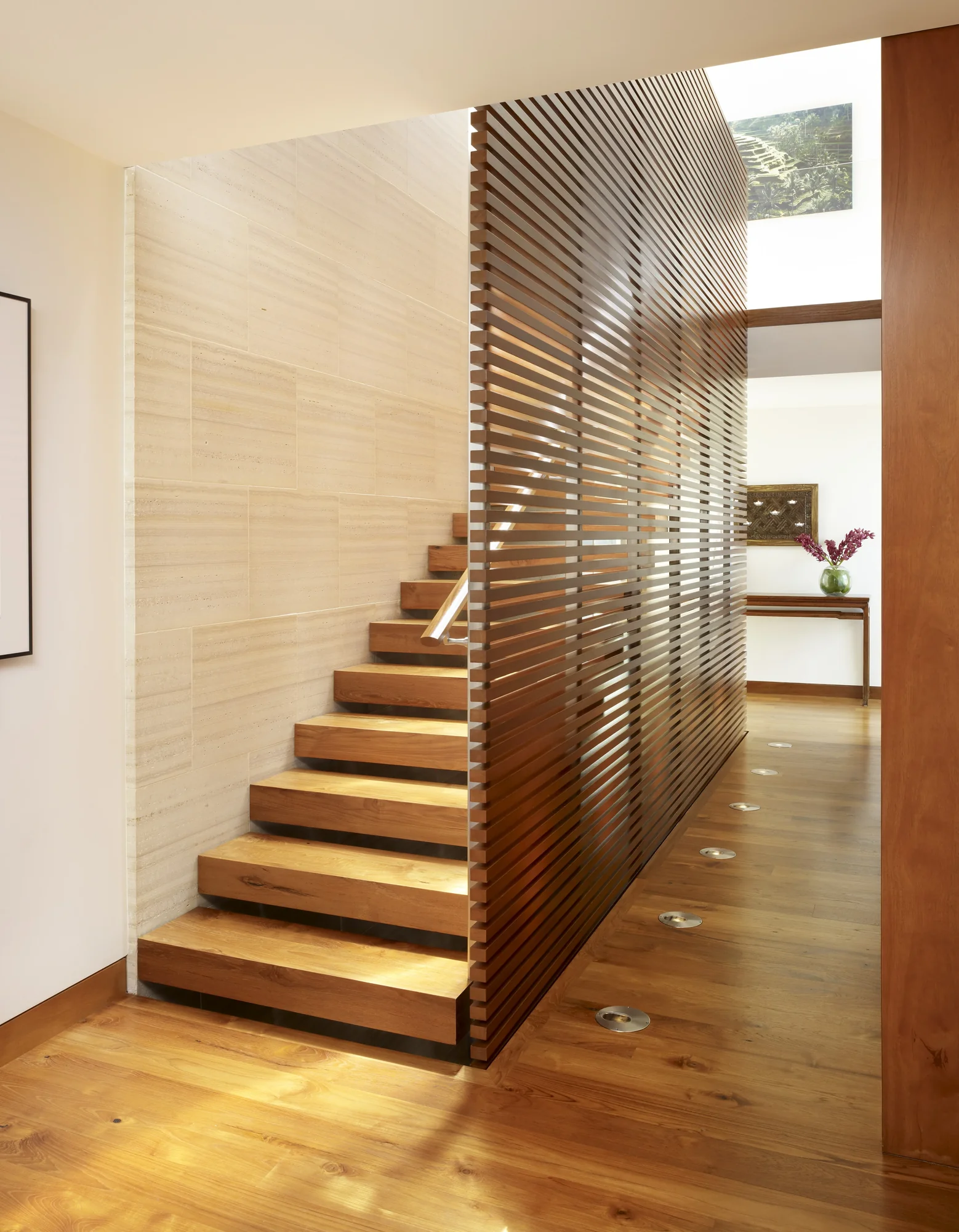 Floating wooden staircase with slatted screen wall, illuminated steps, and natural wood finishes