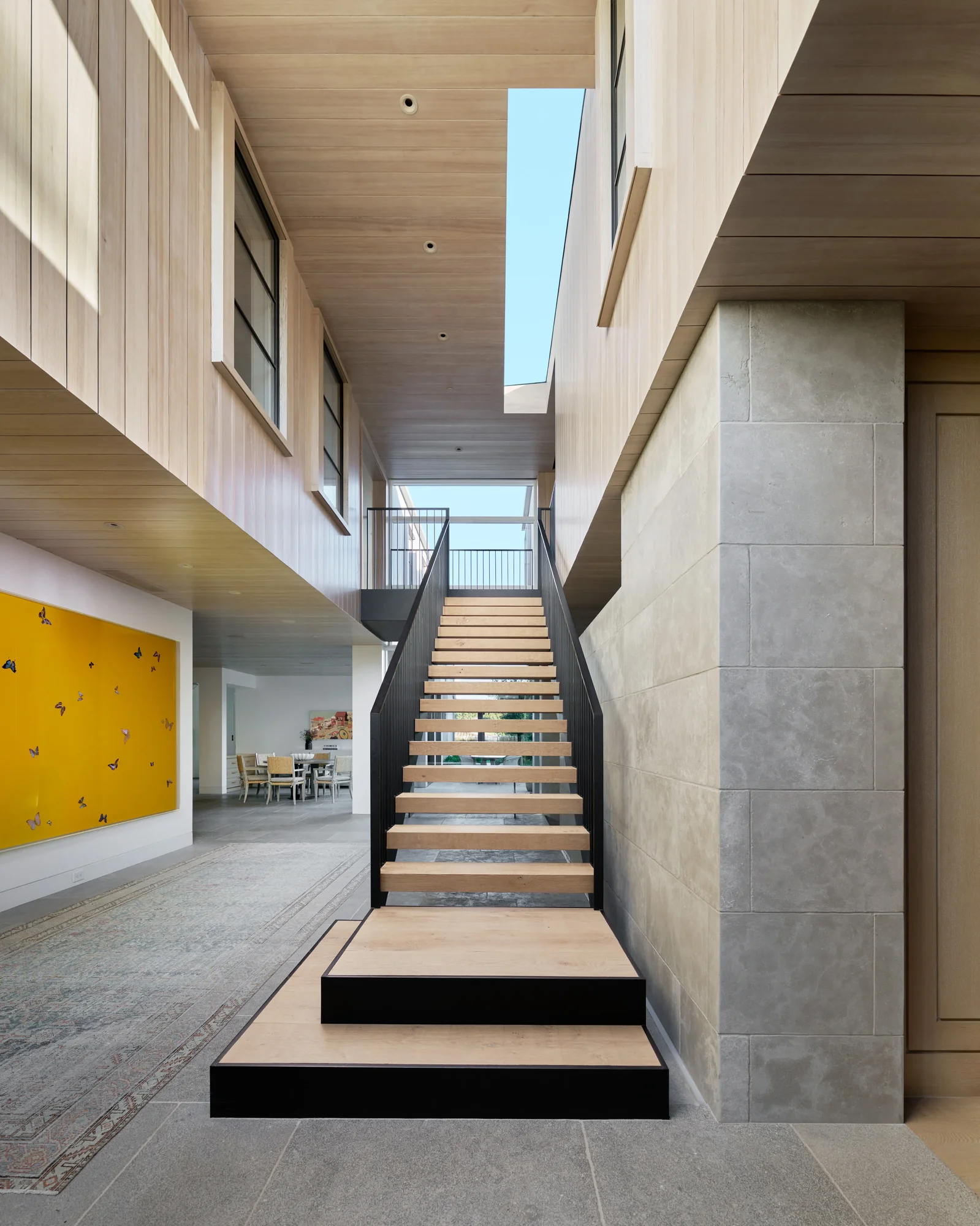 Modern open staircase with wood treads and black steel frame beneath wood ceiling and skylight in contemporary home
