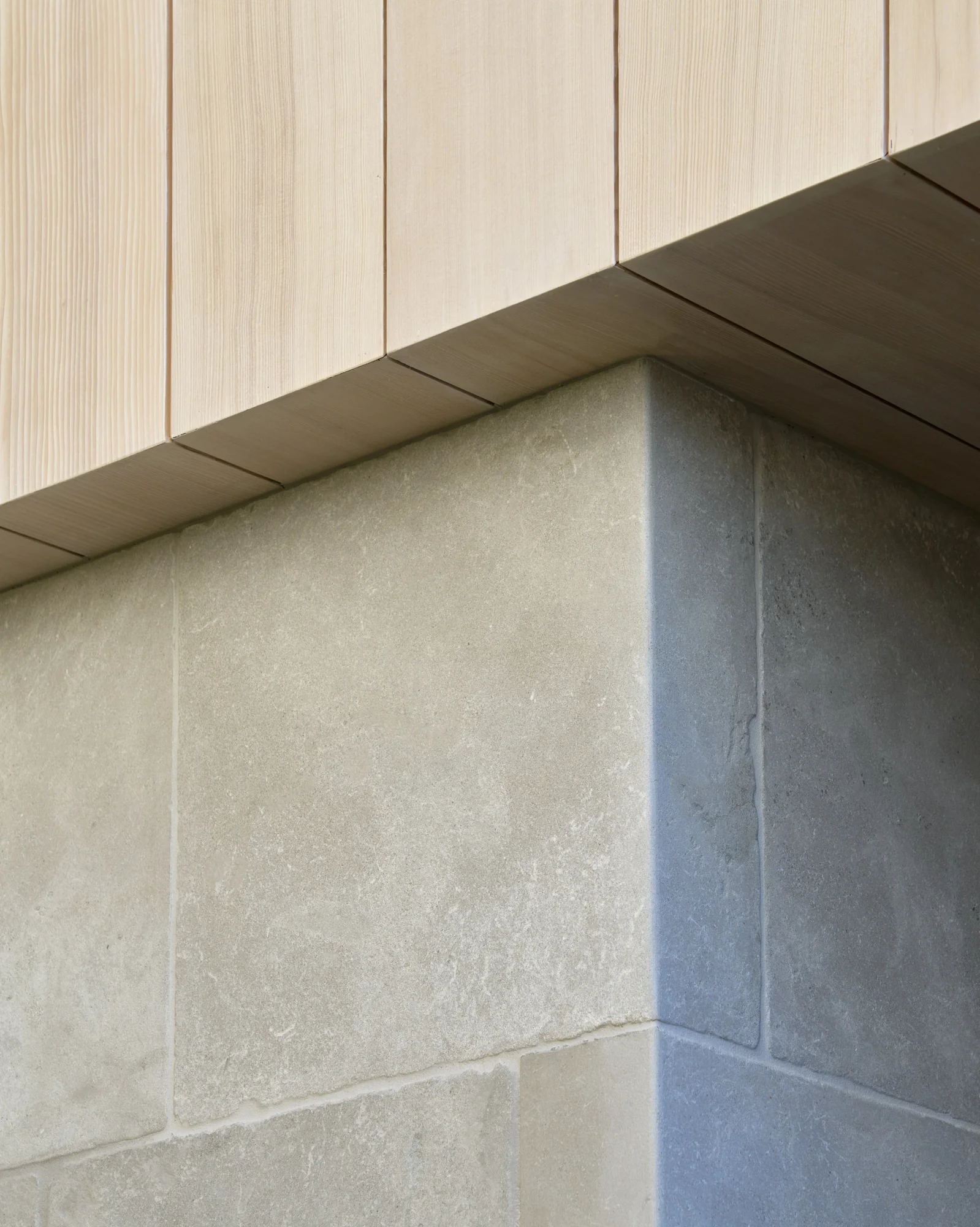 Corner detail showing light stone tile meeting darker stone with dark wood soffit and pale wood paneling above