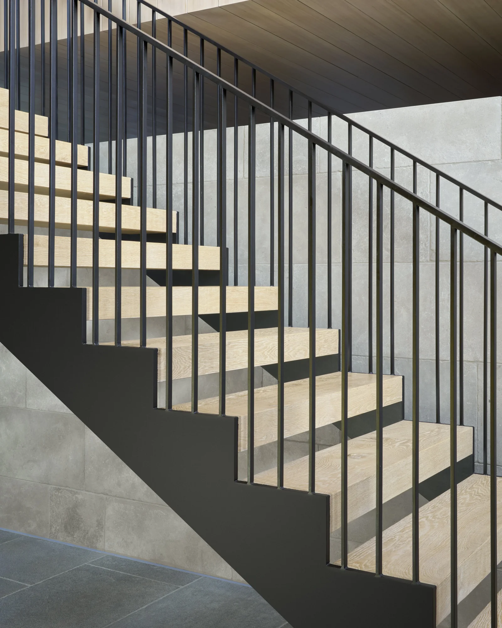 Modern staircase with black steel railings, light wood treads, and concrete walls in contemporary home interior.