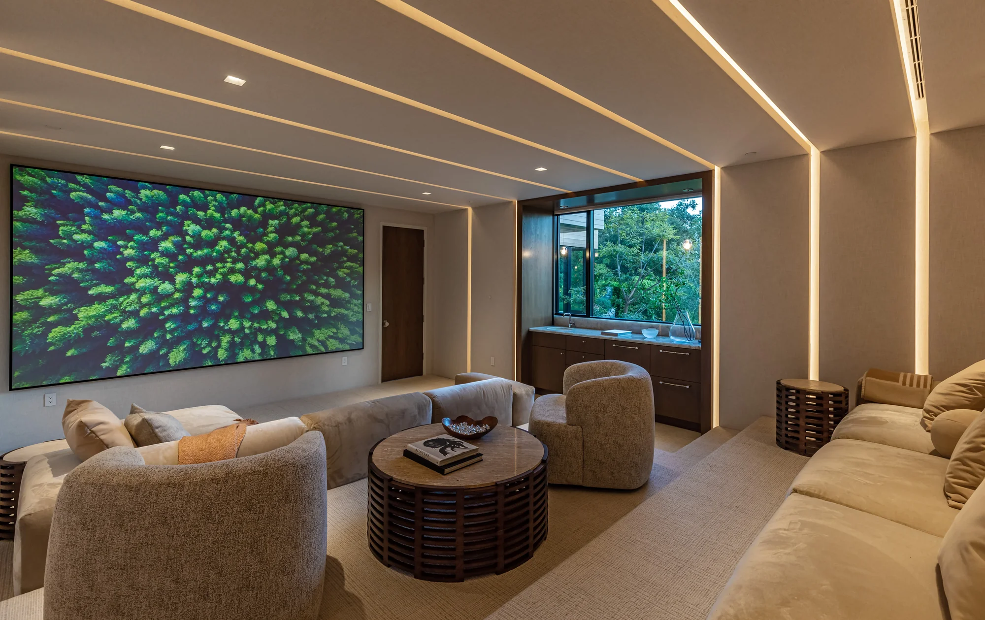 Luxurious home theater with warm linear ceiling lighting, mahogany built-ins, and a large screen beside a lush garden window.