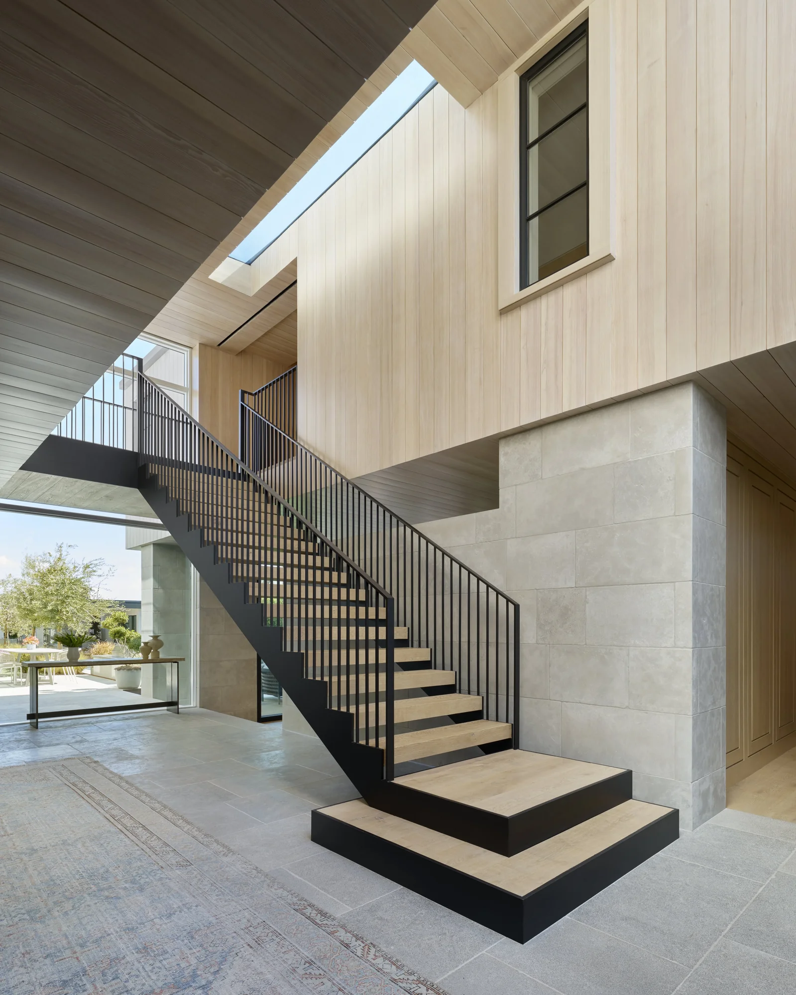 Modern staircase with black steel frame and light wood treads under skylight, featuring vertical metal railings