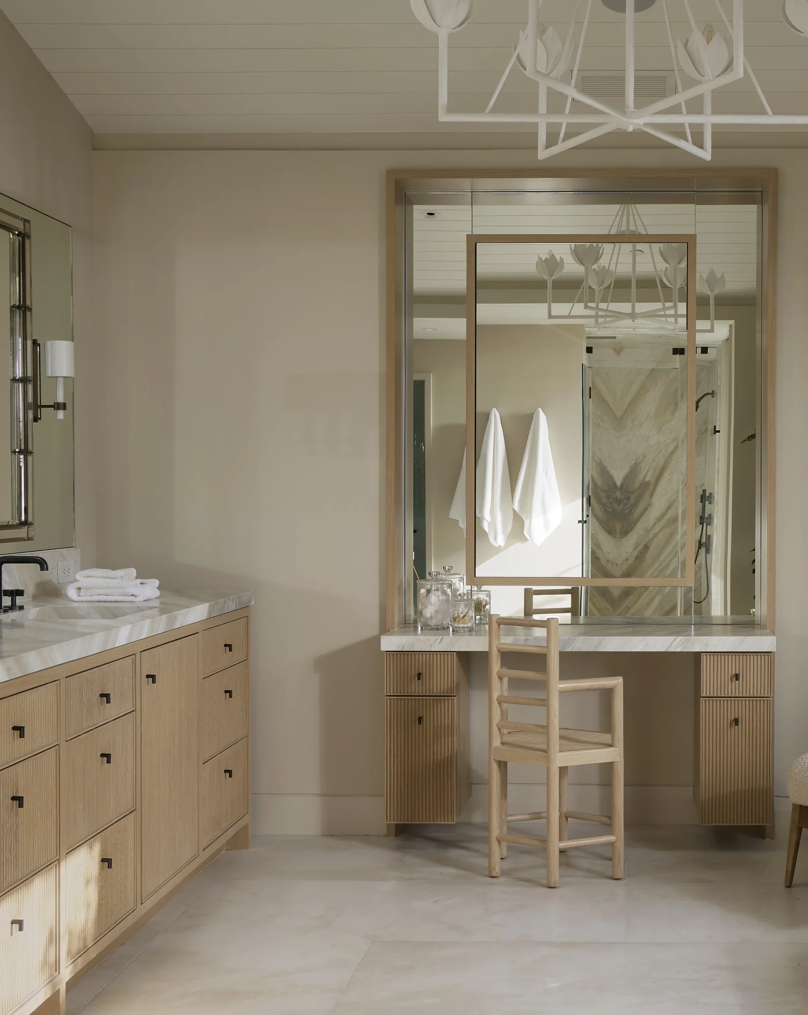 Spa-like bathroom with natural oak vanity, marble countertops, and white chandelier creating a serene, elegant space.