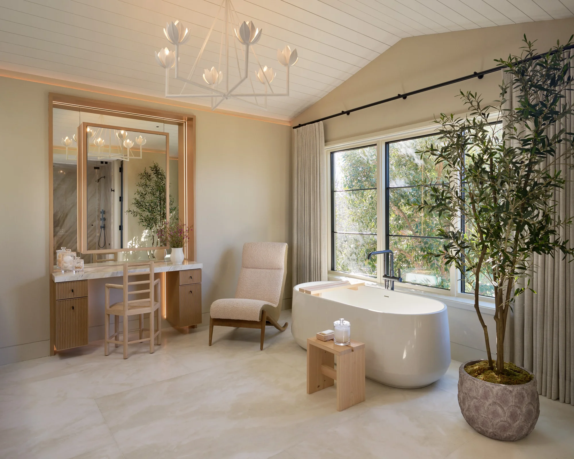 Spa-like bathroom with freestanding white tub, natural light, indoor olive tree, and illuminated vanity with mirror