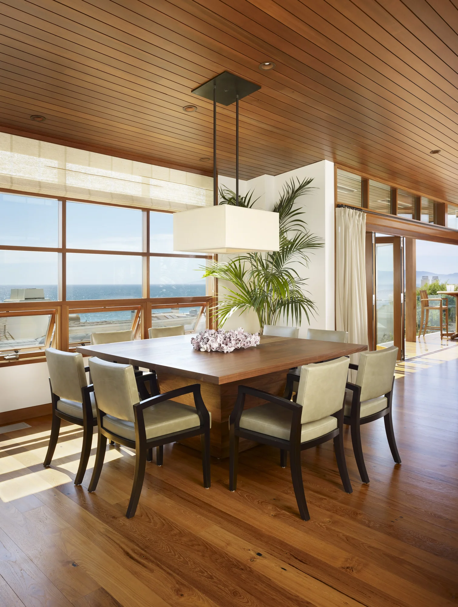 Modern dining room with wood ceiling, ocean views, and natural materials connecting indoor and outdoor spaces