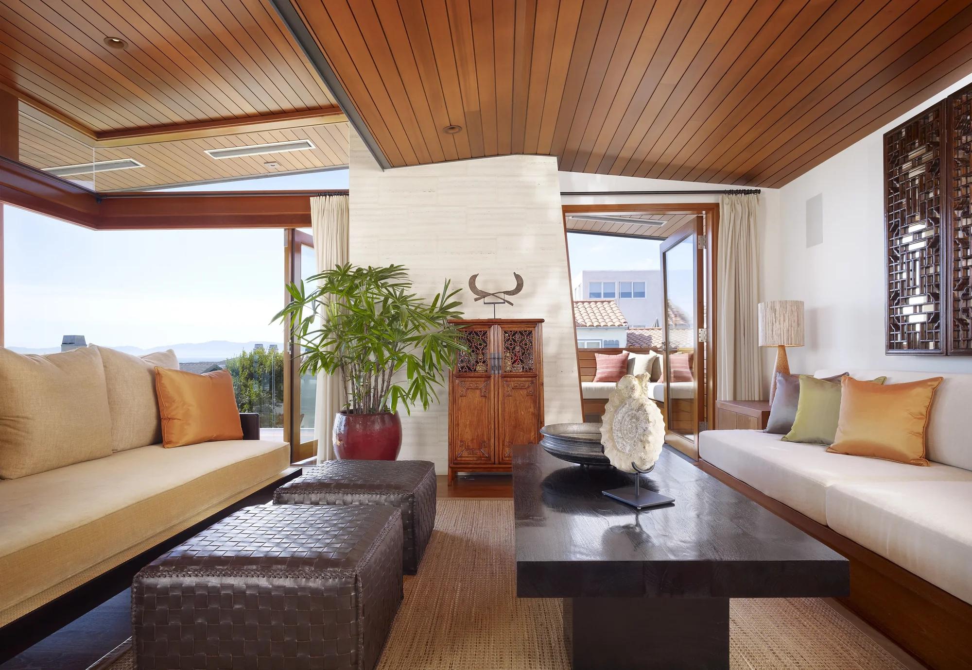 Modern living room with wood ceiling, built-in sofas, natural light, and indoor-outdoor connection through open doorways.