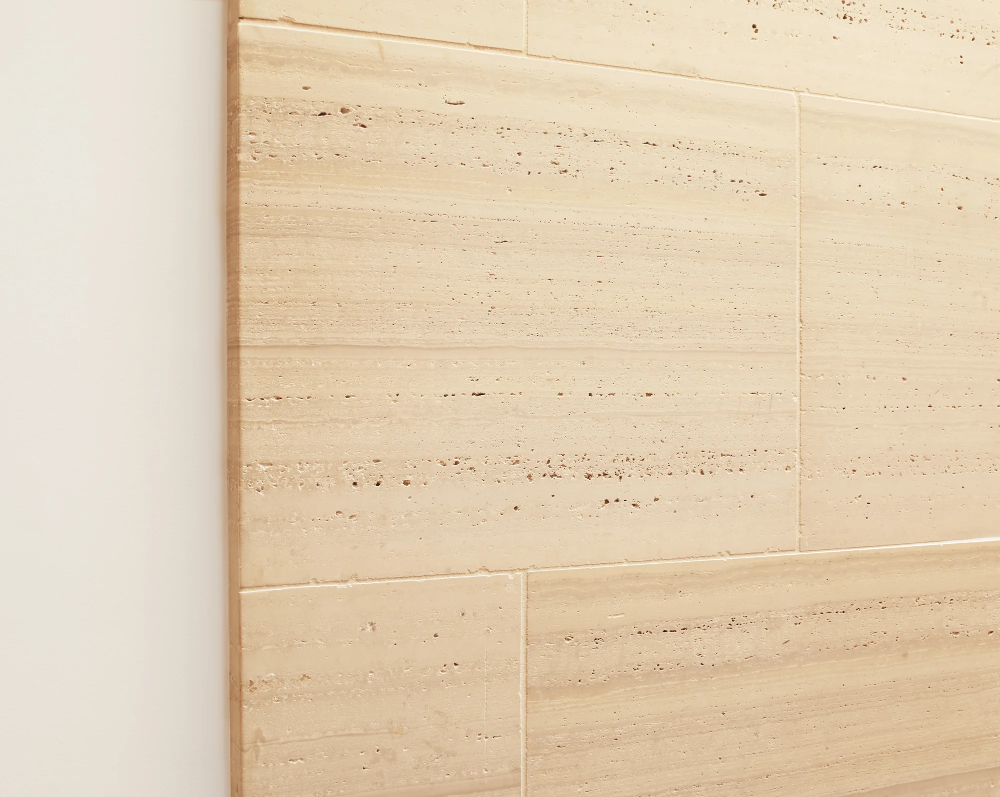 Close-up of travertine stone tile wall showing natural veining, texture, and warm beige tones with grout lines.