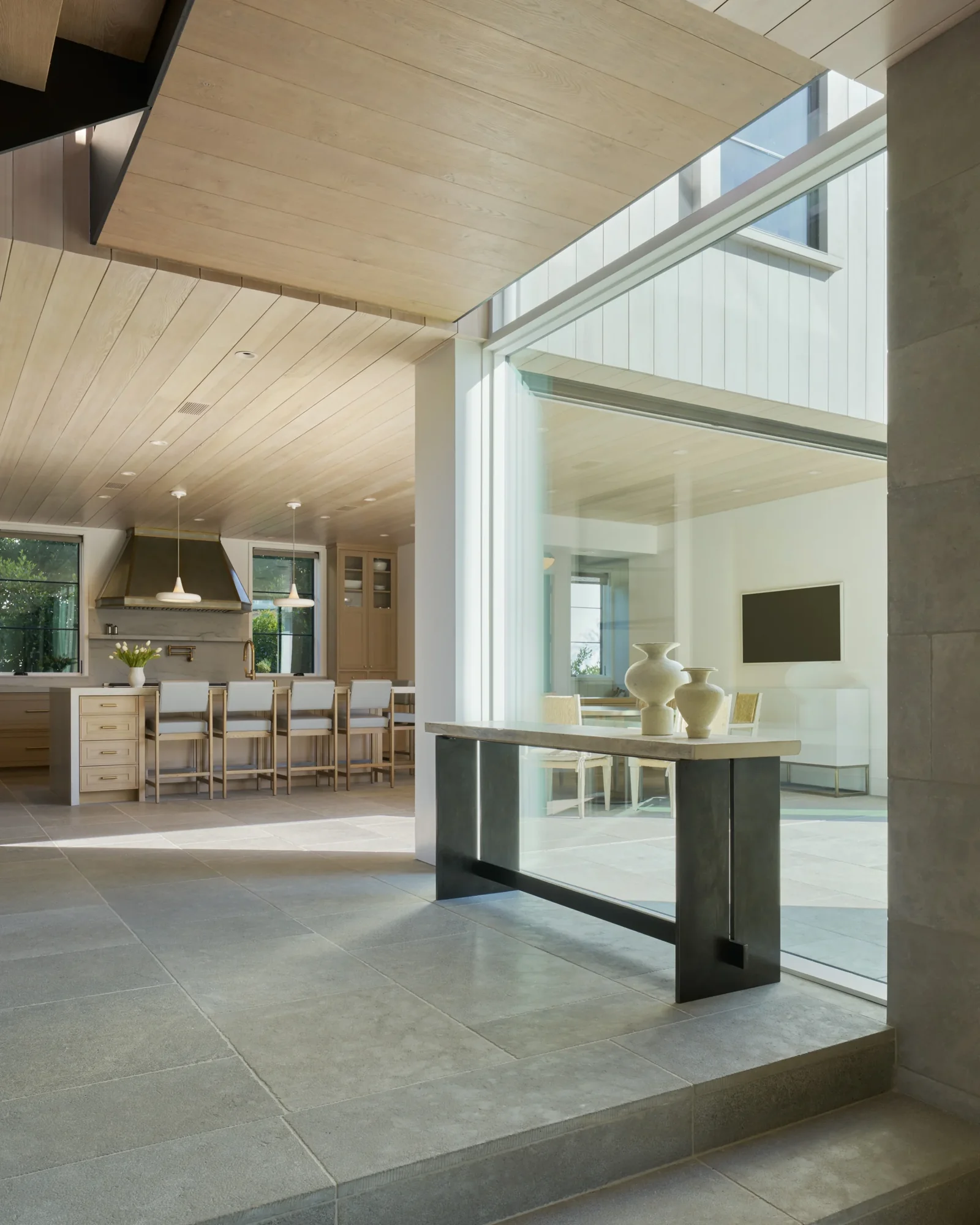 Open-plan living space with natural wood ceilings, stone floors, and seamless indoor-outdoor connection through glass walls