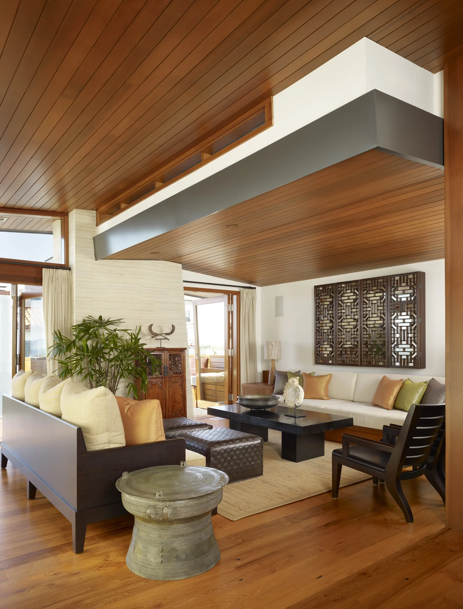 Modern living room with wood ceiling, seating areas, and decorative wall panel showcasing indoor-outdoor flow