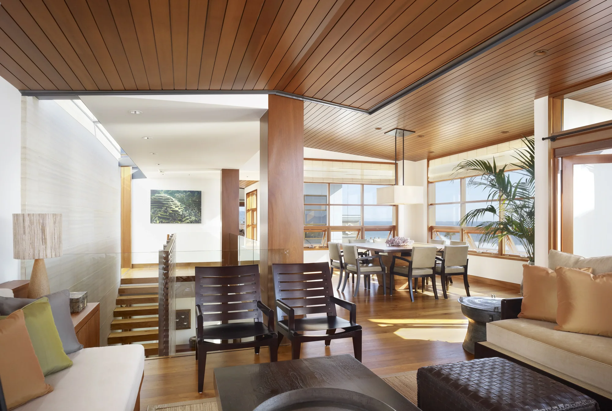 Open-plan living space with wood slat ceiling, natural light, and seamless flow between sitting and dining areas.