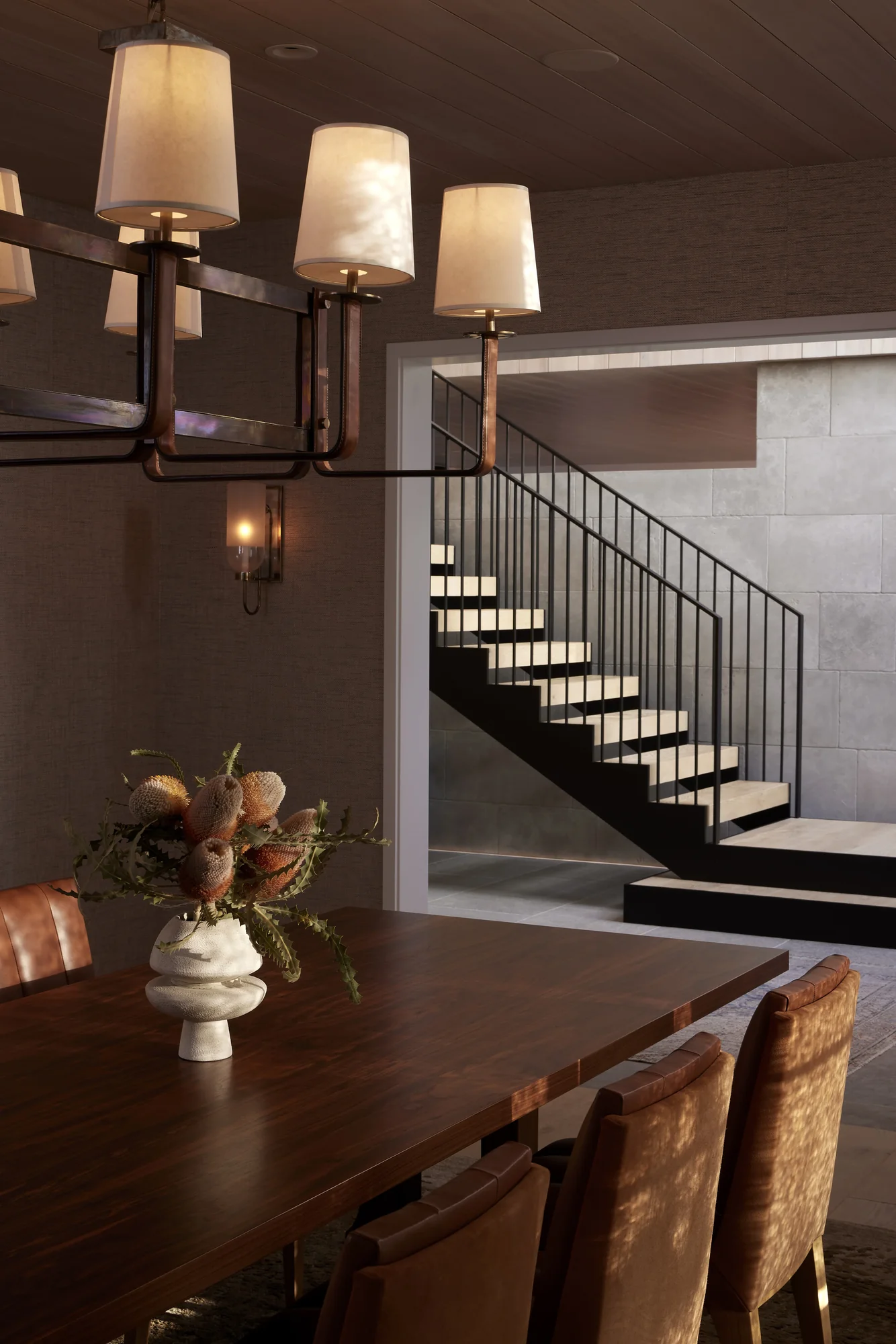 Modern dining room with dark wood table, chandelier with fabric shades, and floating staircase with metal railings