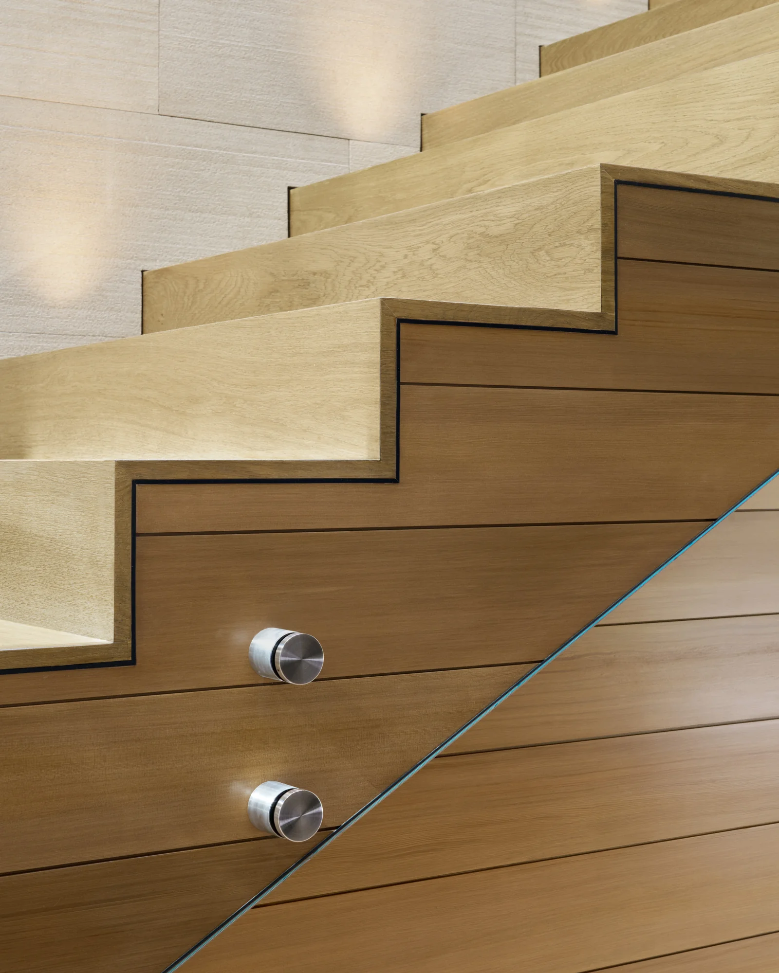 Close-up of white oak stair treads with a glass balustrade panel secured by polished stainless steel standoffs.