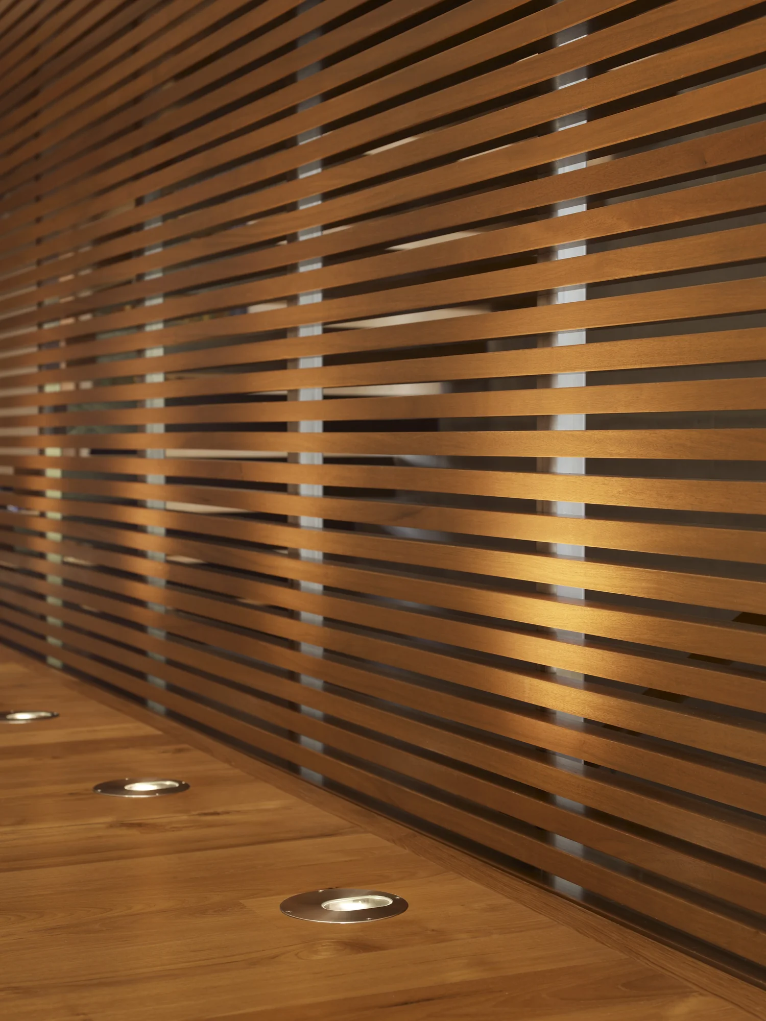 Curved wooden slat wall with recessed floor lighting creating warm ambient illumination in modern interior space