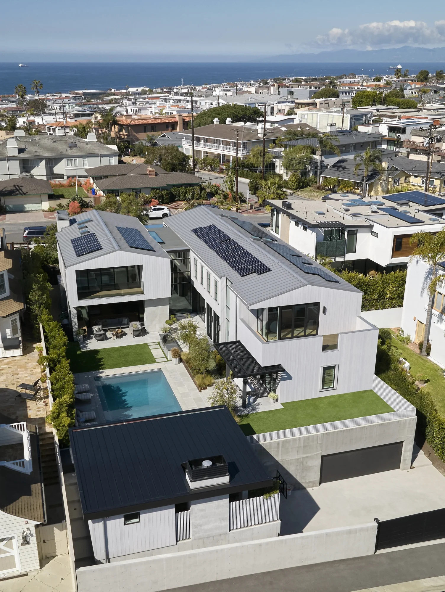 Aerial view of modern white coastal homes with solar panels, overlooking ocean and neighboring community