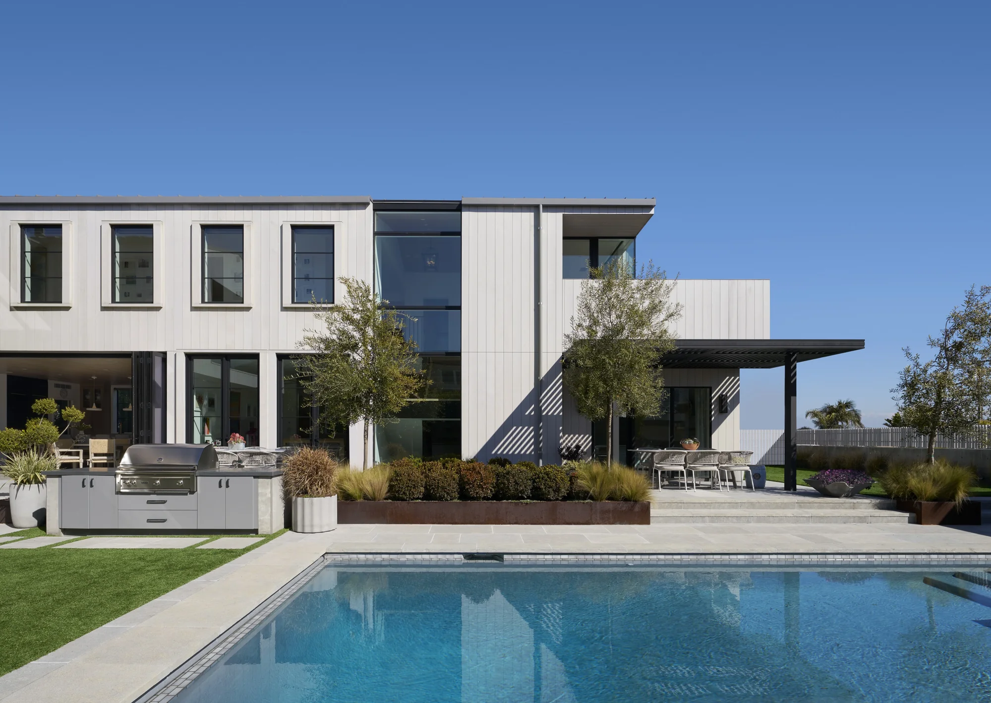 Modern white home with pool, outdoor kitchen, and covered patio featuring natural materials and indoor-outdoor living