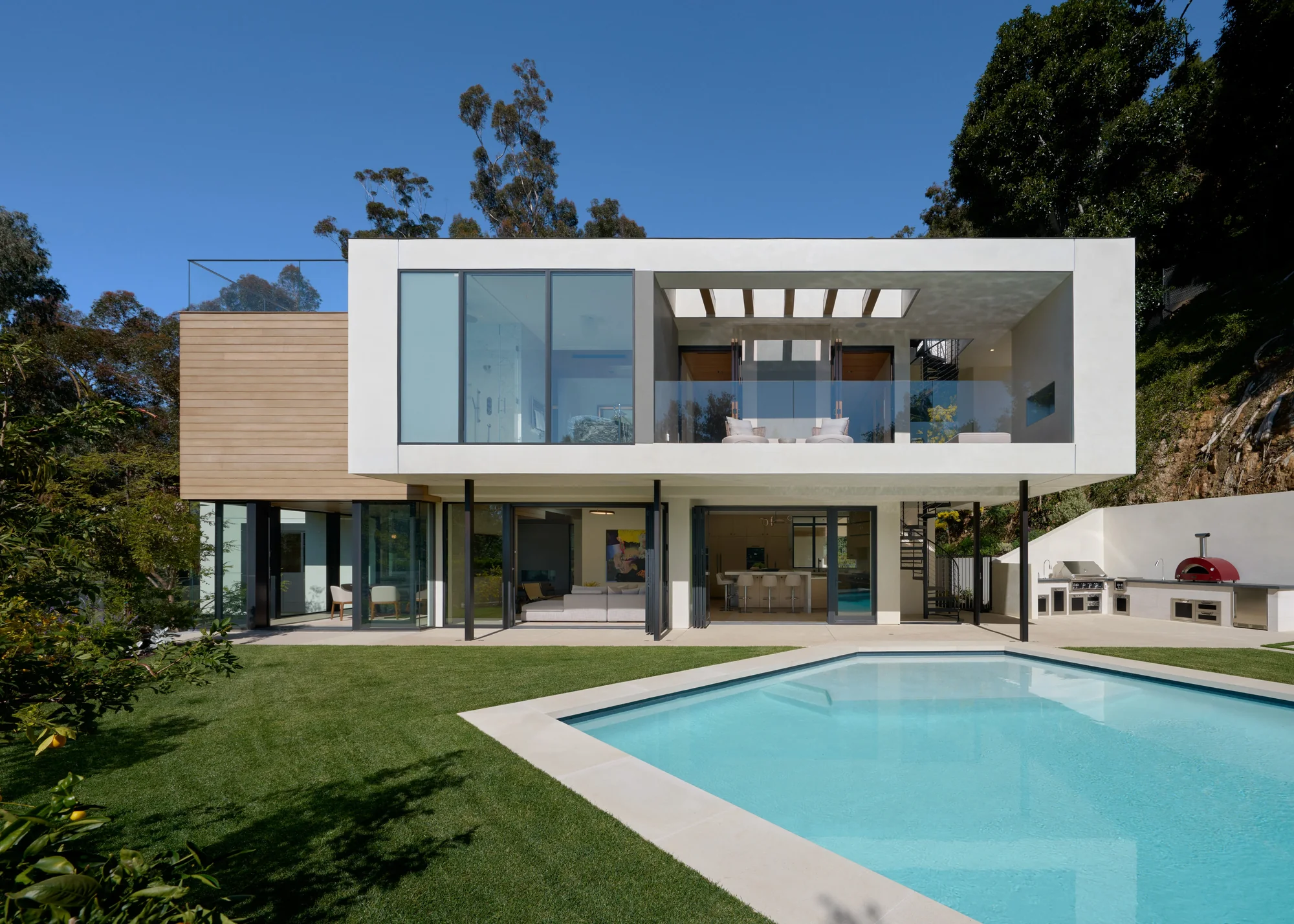 Modern two-story home with cedar cladding, floor-to-ceiling glass, open-air terrace, and pool seamlessly connecting indoors to outdoors.